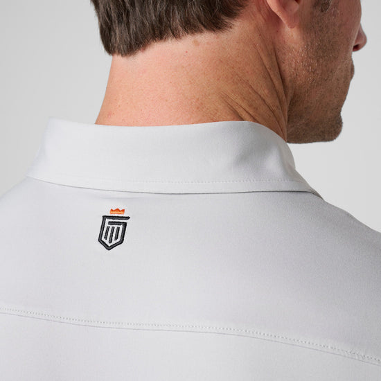 White polo shirt with collared neckline and small embroidered shield logo on back.