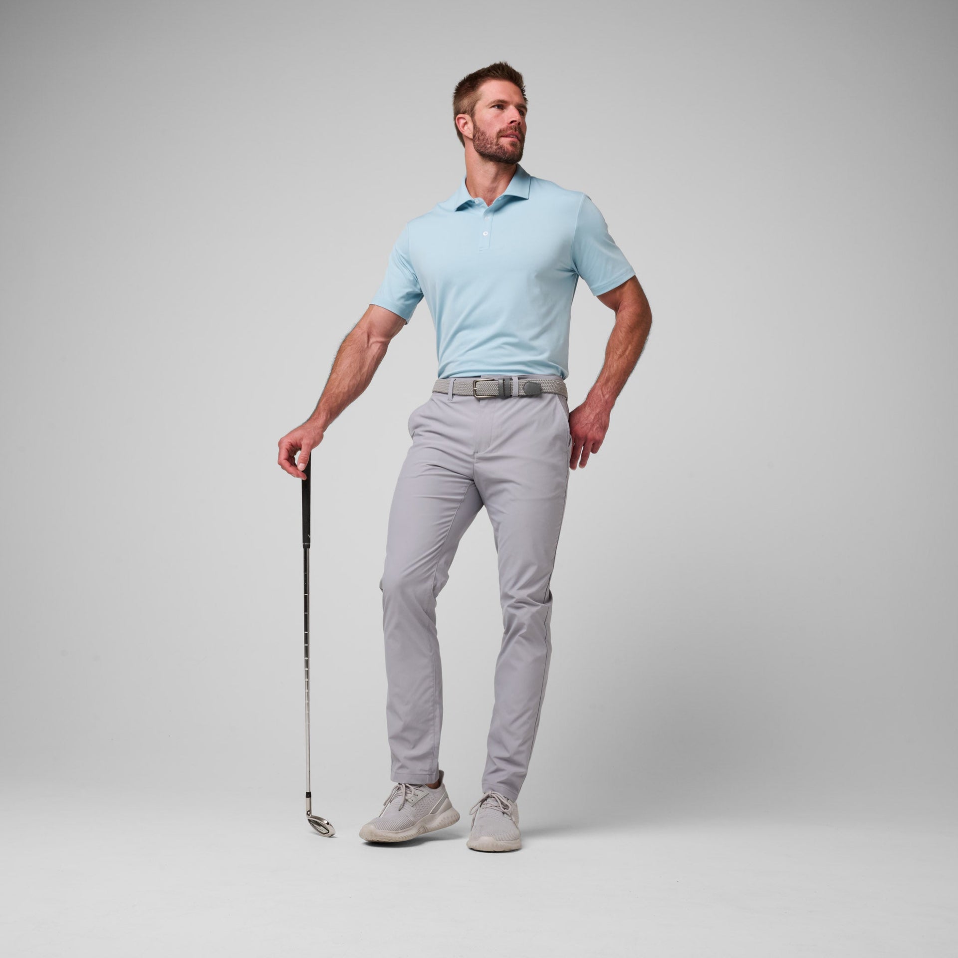 Man wearing light blue short-sleeve polo shirt with gray pants and belt, holding a golf club.