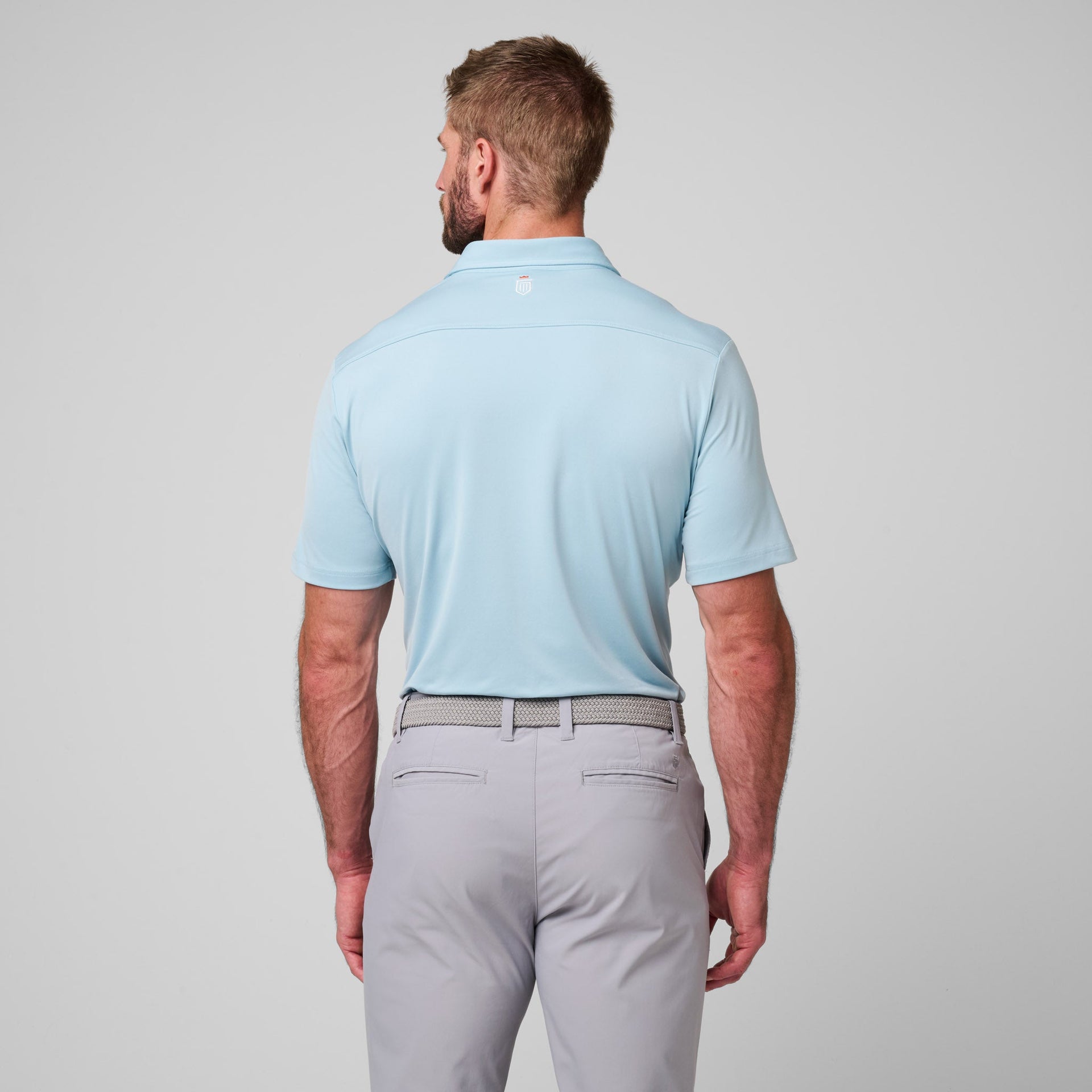 Man wearing light blue short-sleeve polo shirt with gray pants and woven belt, shown from back view.