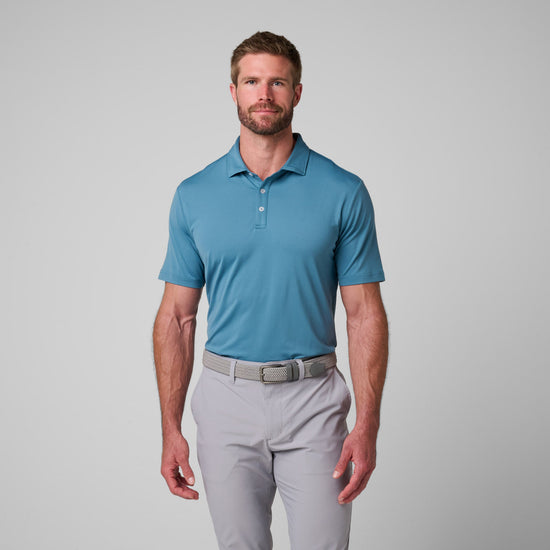 Man wearing blue short-sleeve polo shirt with collar and button placket, paired with light gray pants and beige belt.