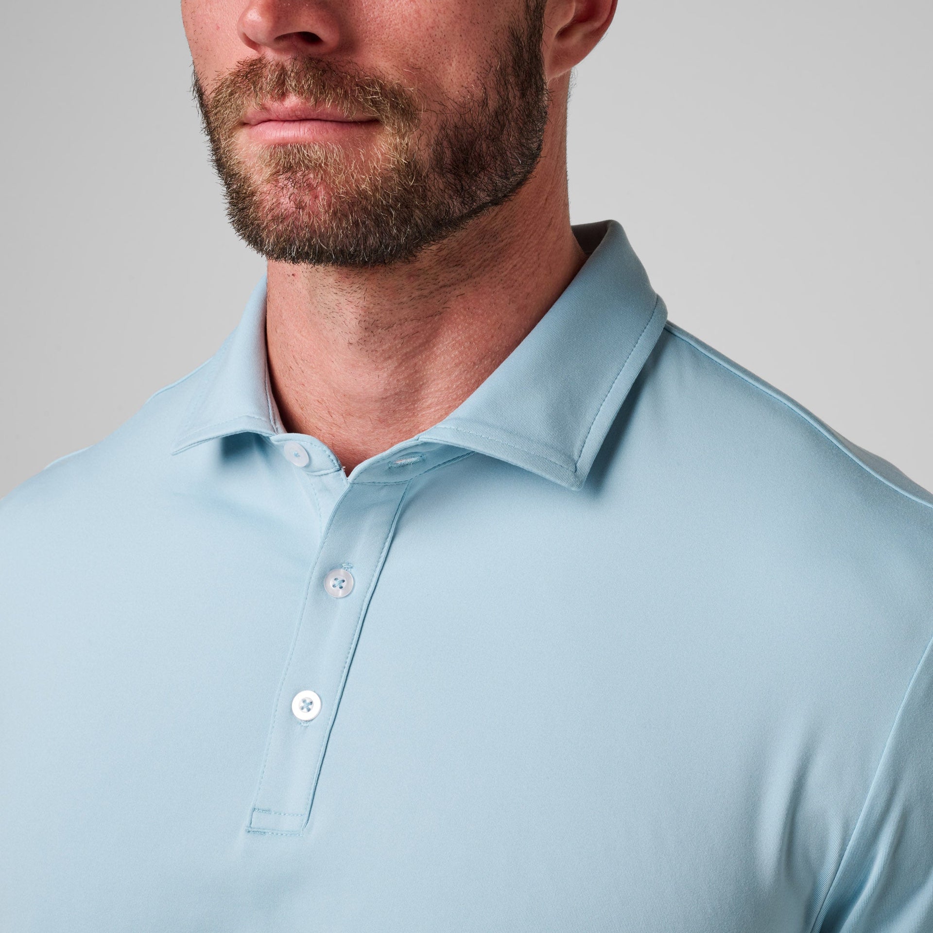 Light blue polo shirt with white buttons and collar, worn by man with beard against neutral background.