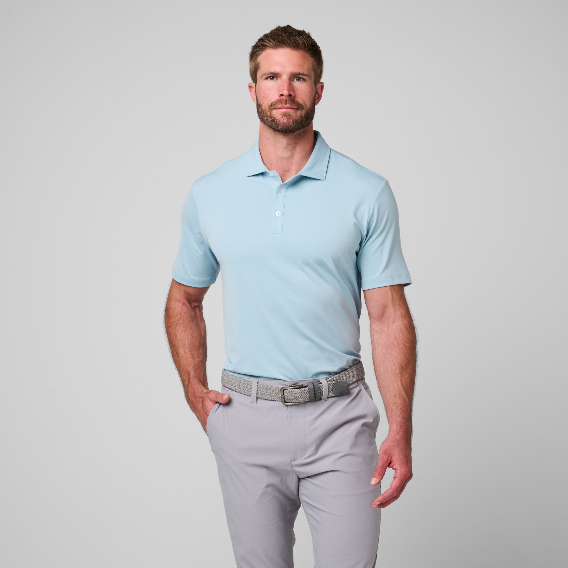 Light blue short-sleeve polo shirt with collar and white button placket worn with gray pants and tan belt.