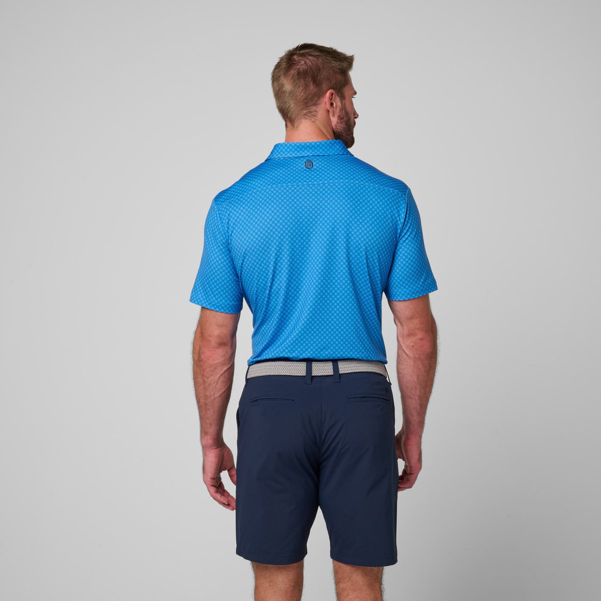 Blue printed polo shirt with geometric pattern, shown from back on model wearing navy shorts.