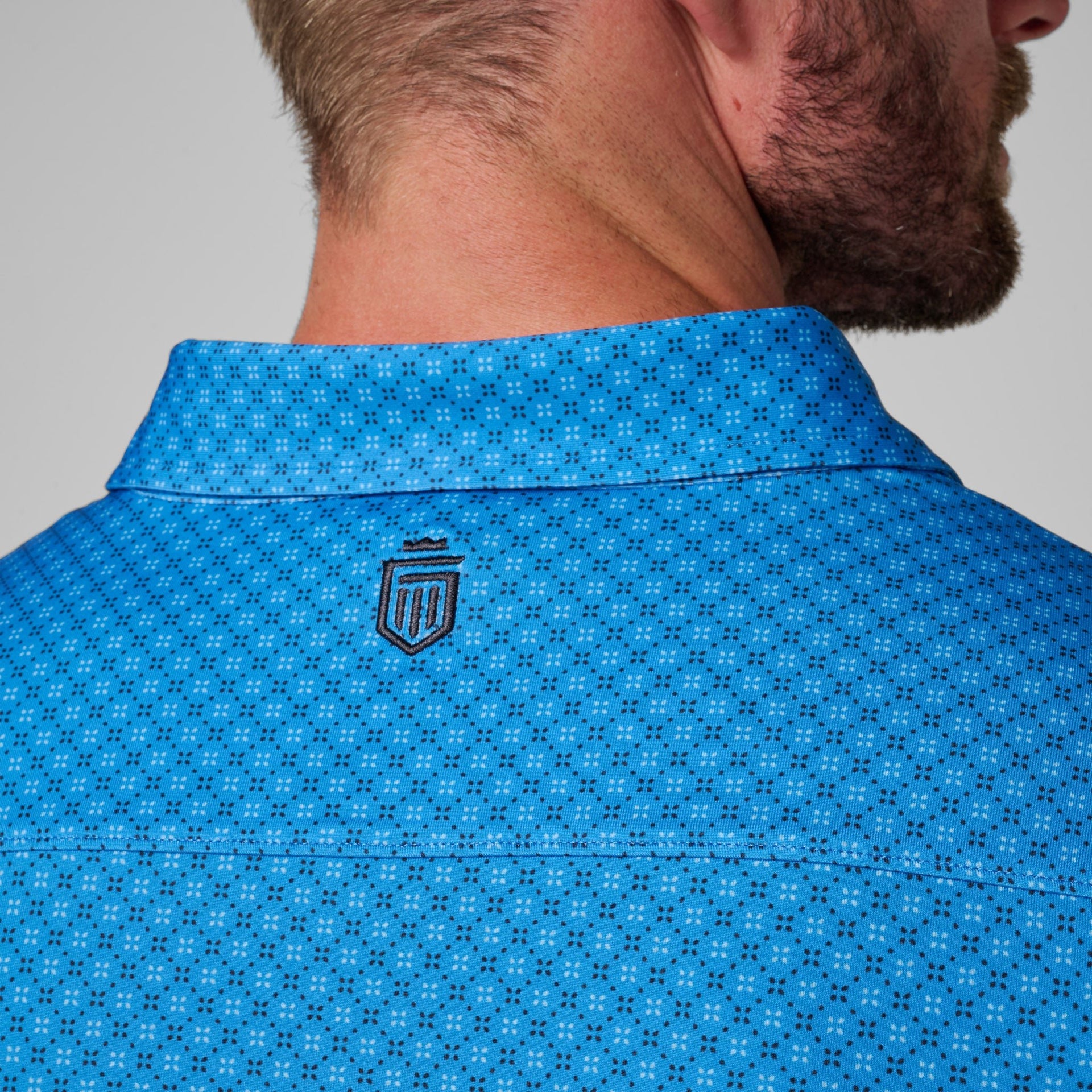 Man wearing bright blue polo shirt with small geometric pattern and embroidered logo on back neck.