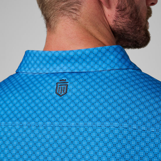 Man wearing bright blue polo shirt with small geometric pattern and embroidered logo on back neck.