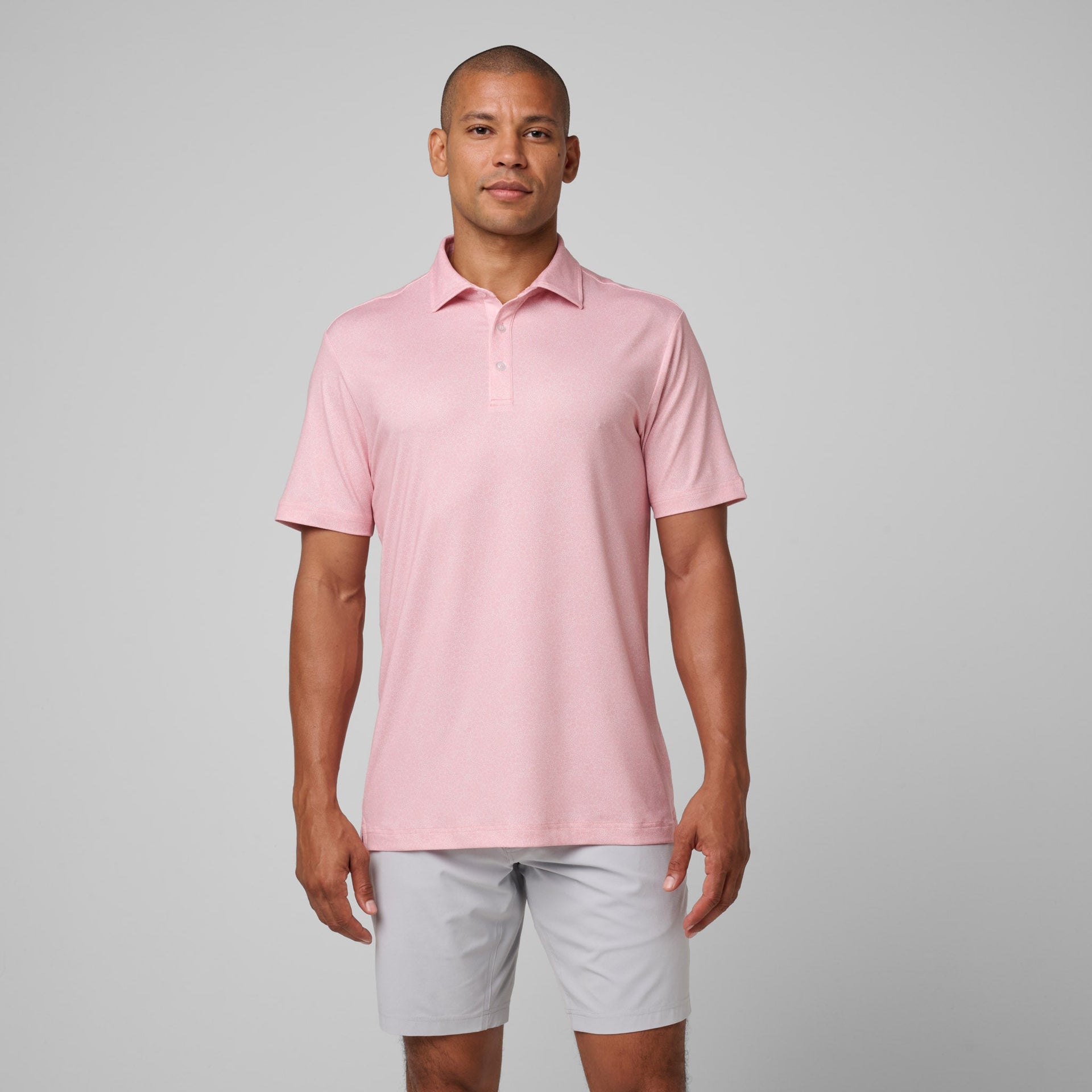 Man wearing pink short-sleeve polo shirt with white button placket and gray shorts.