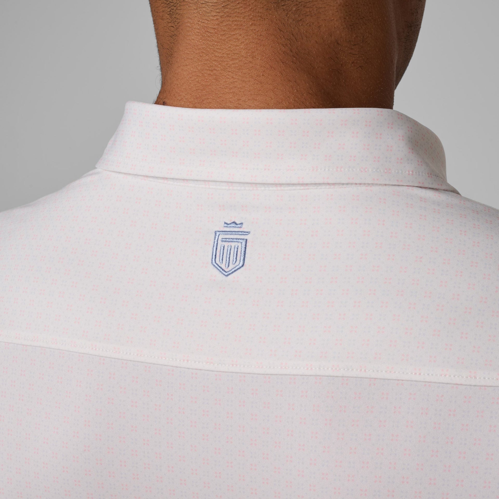 Light pink polo shirt with blue shield logo embroidered on back neck.
