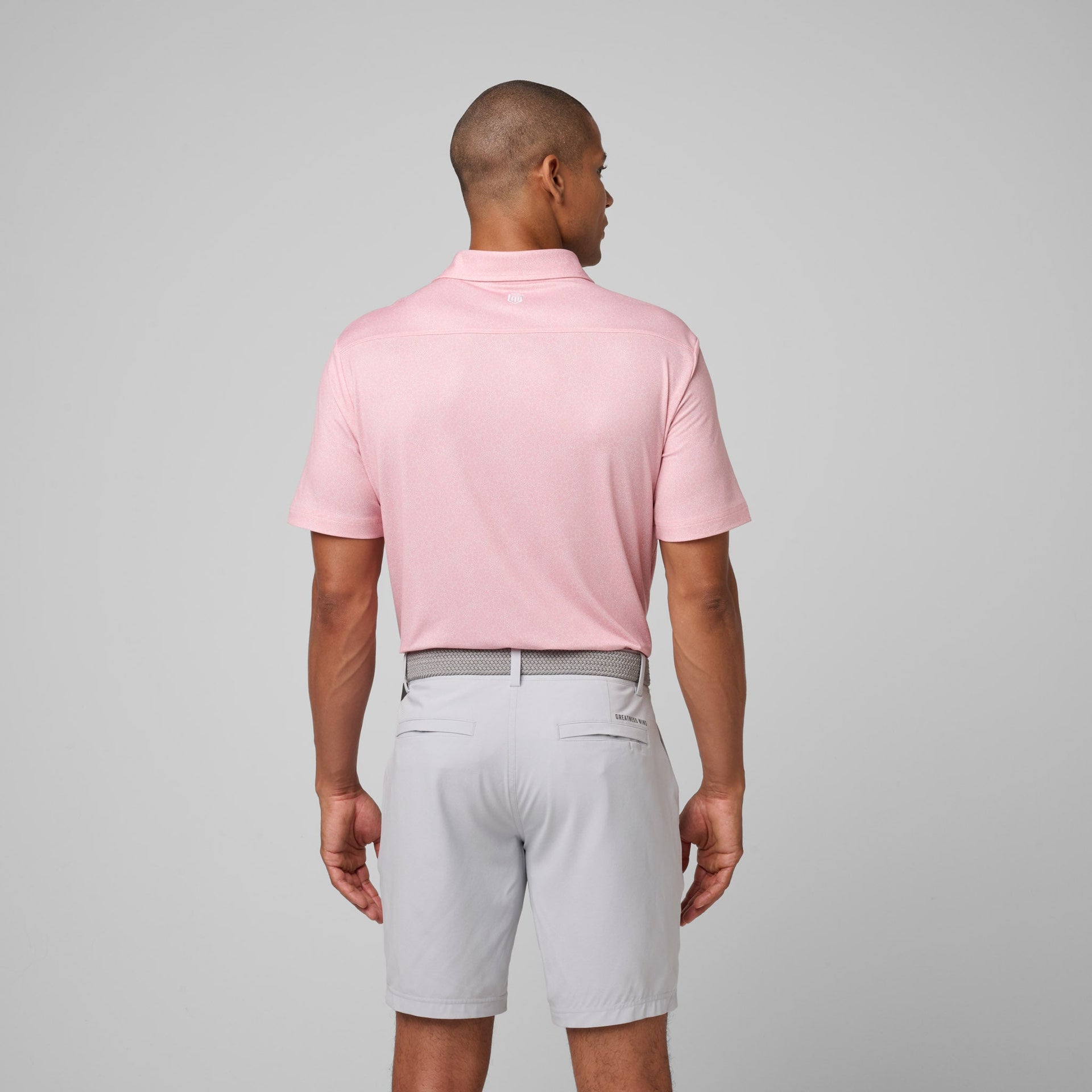 Man wearing light pink short-sleeve polo shirt and white shorts with gray patterned belt, shown from back.