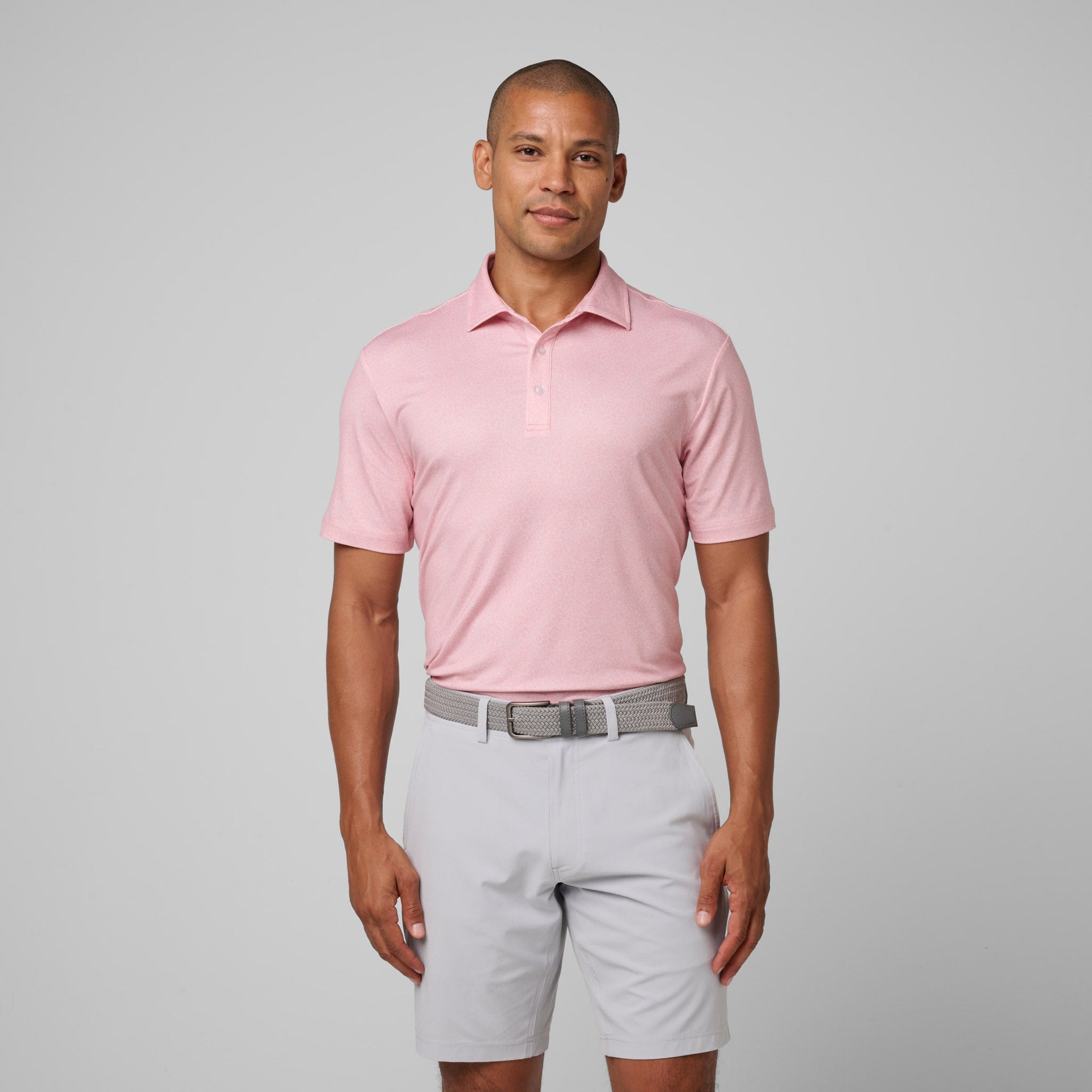 Man wearing pink short-sleeve polo shirt with white shorts and gray woven belt.