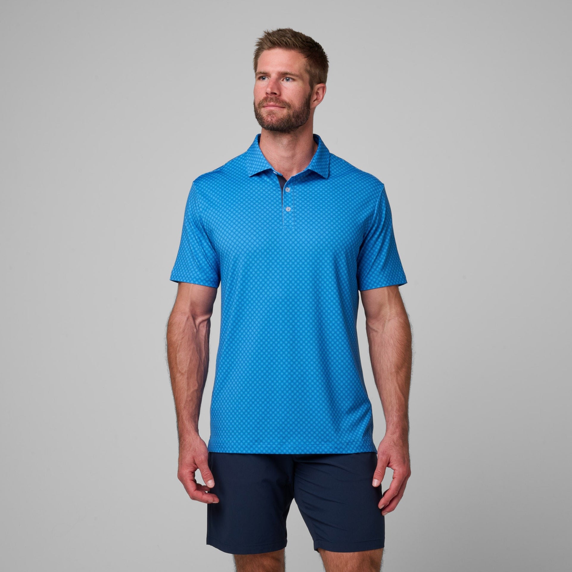 Blue polo shirt with geometric print pattern and collar, worn with navy shorts.