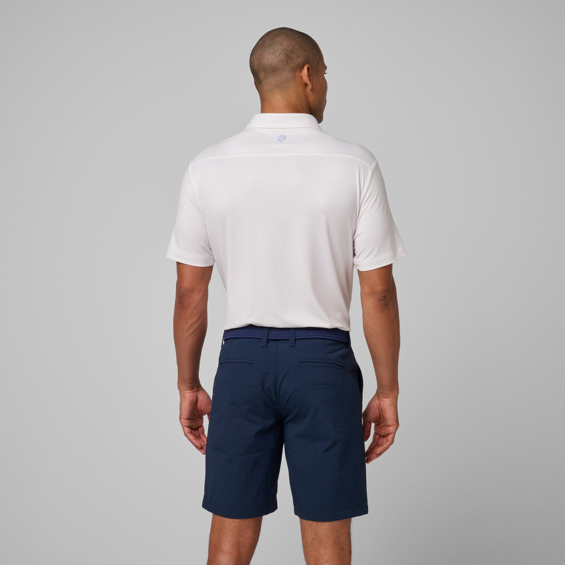 Man wearing white short-sleeve polo shirt with collar and navy shorts, shown from back view.