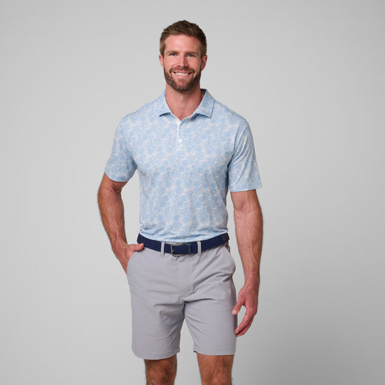 Man wearing light blue printed polo shirt with white buttons and gray shorts with navy belt.