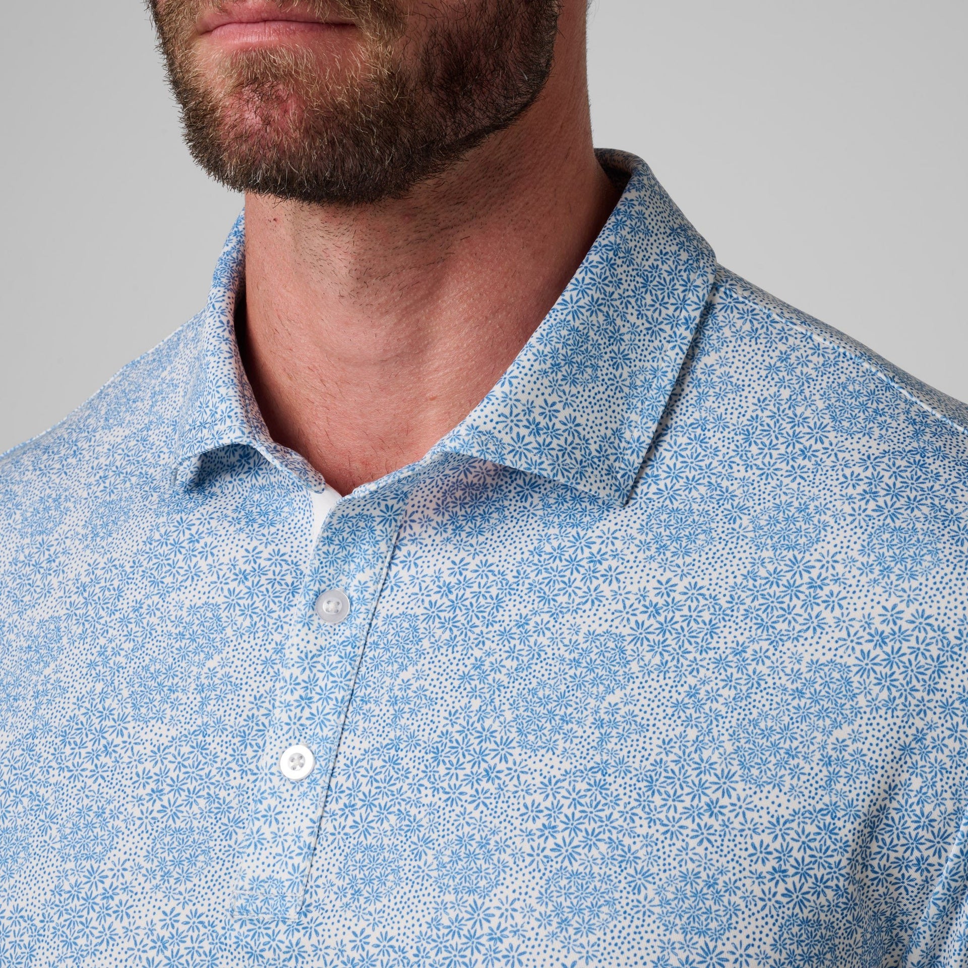 Men's polo shirt with blue geometric print and white buttons, shown from chest up.