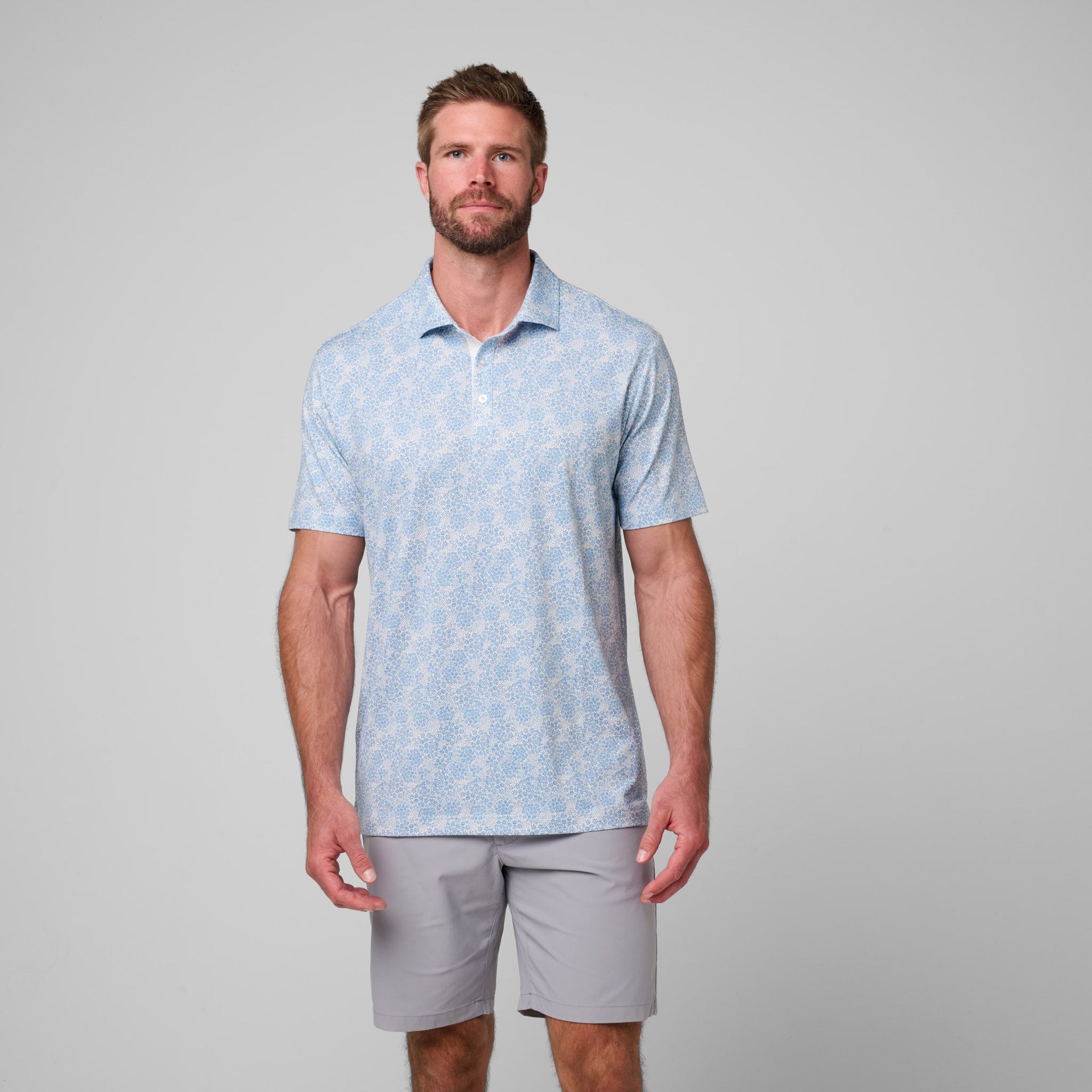 Man wearing light blue printed polo shirt with small geometric pattern and gray shorts.