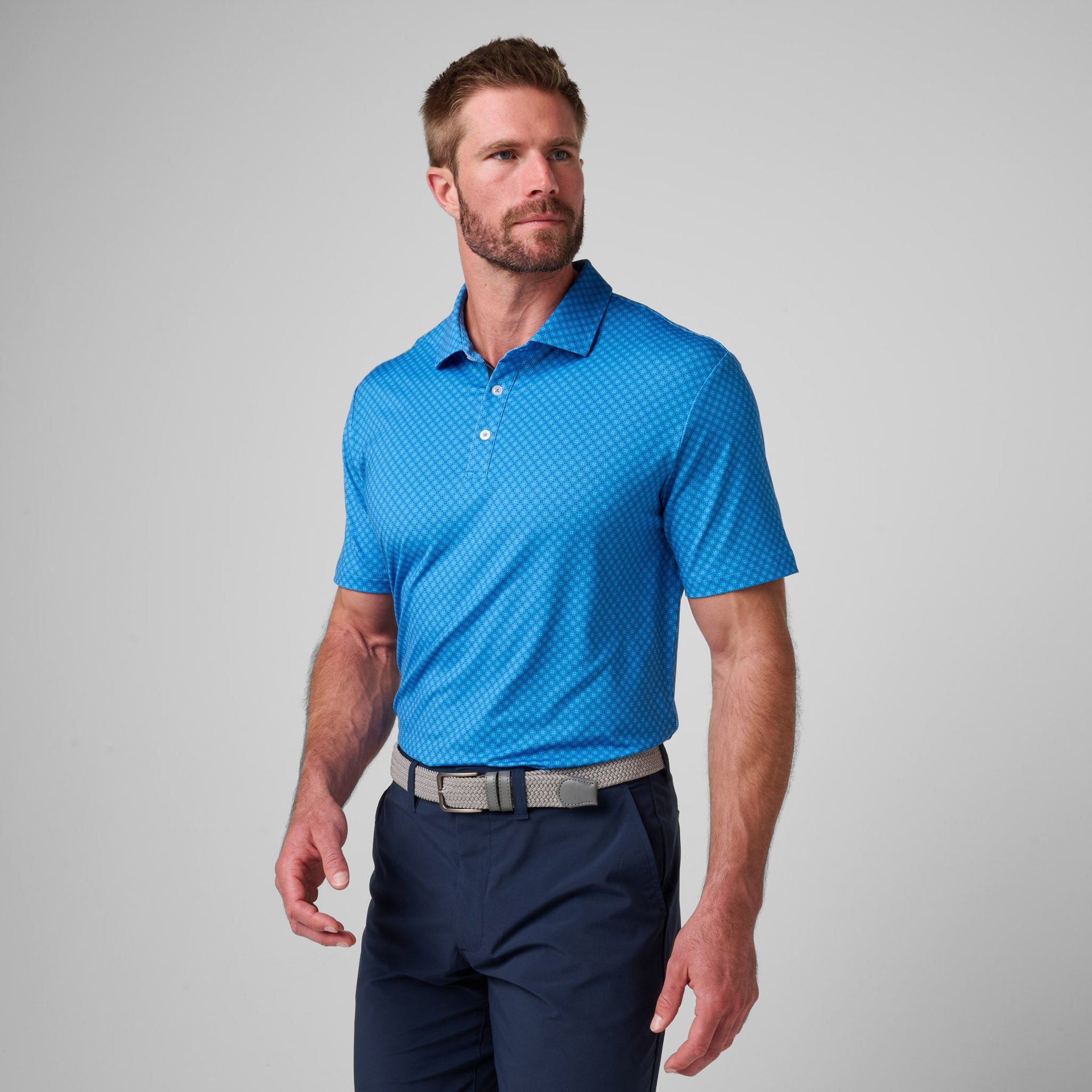 Blue polo shirt with geometric print pattern and white button placket worn with navy pants.