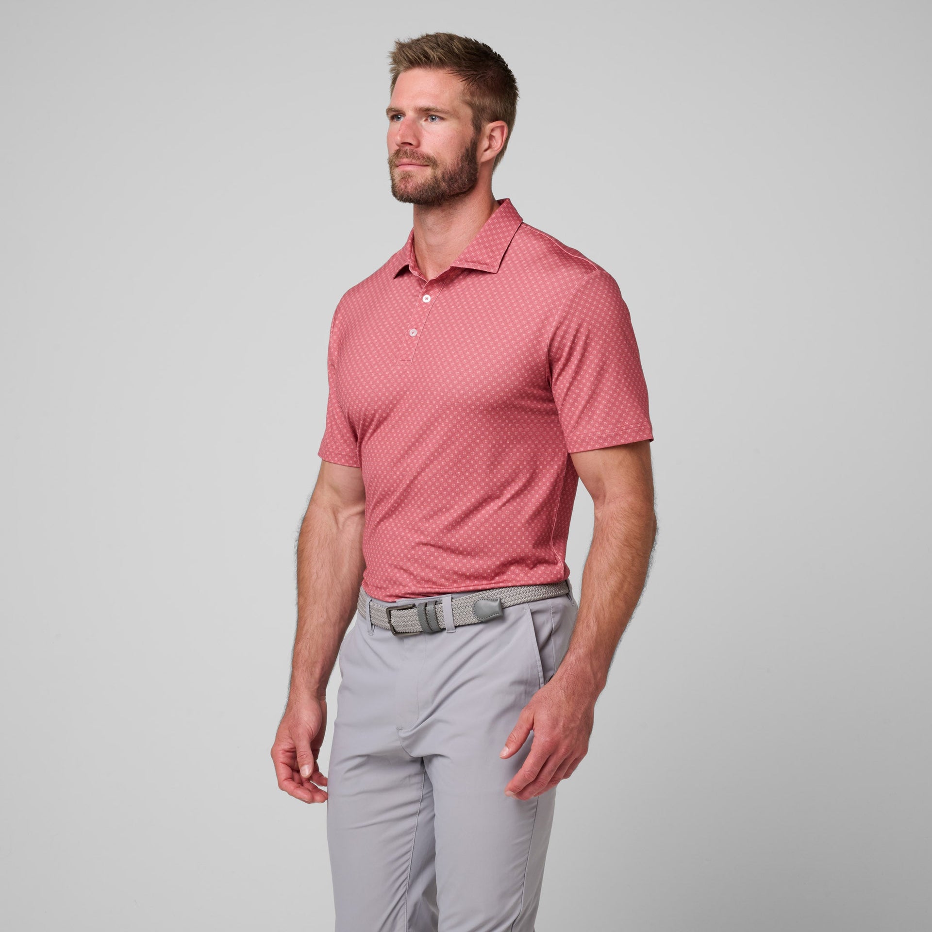 Man wearing pink patterned short-sleeve polo shirt with white buttons and gray pants with belt.