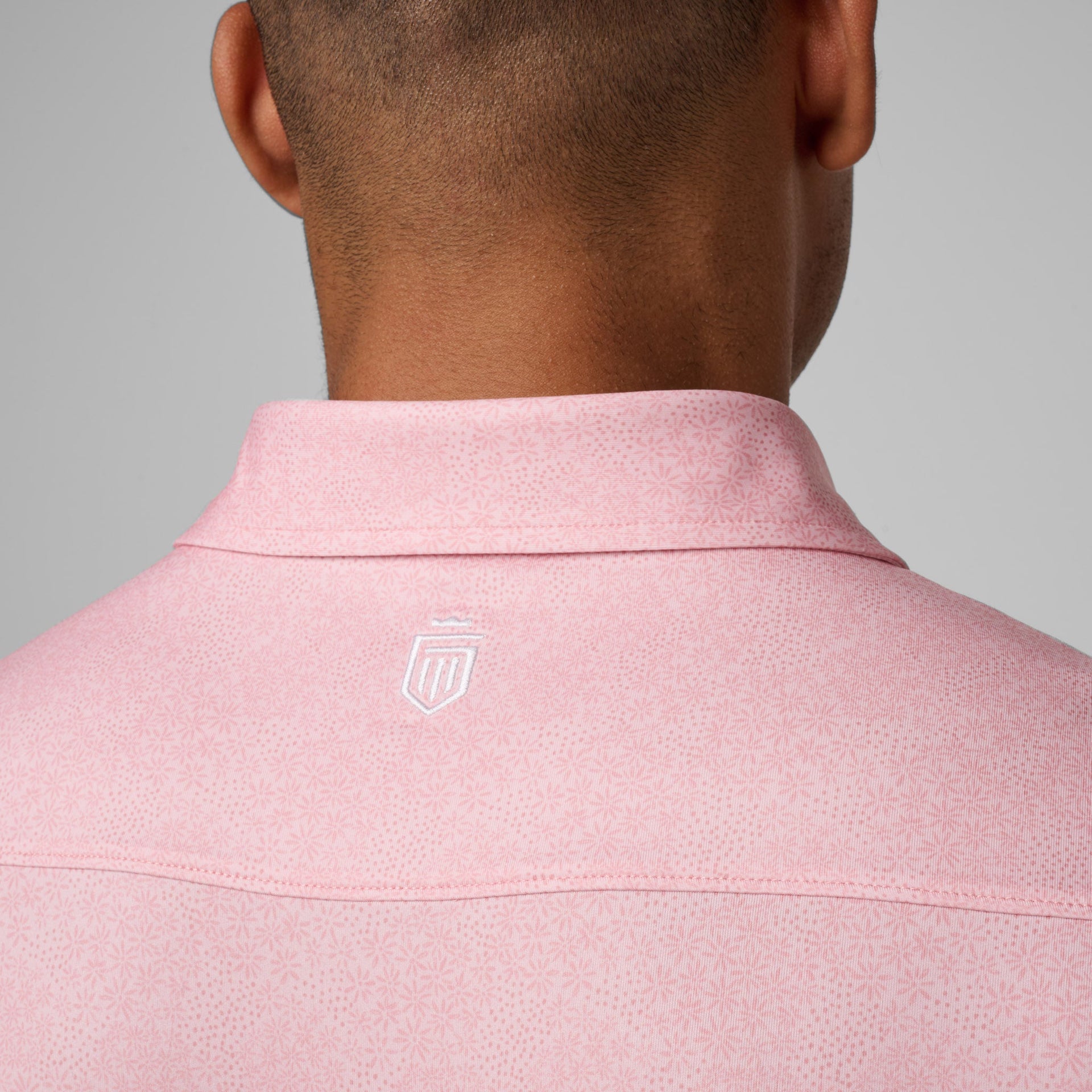 Pink polo shirt with white shield logo on back neck, worn by man shown from behind.