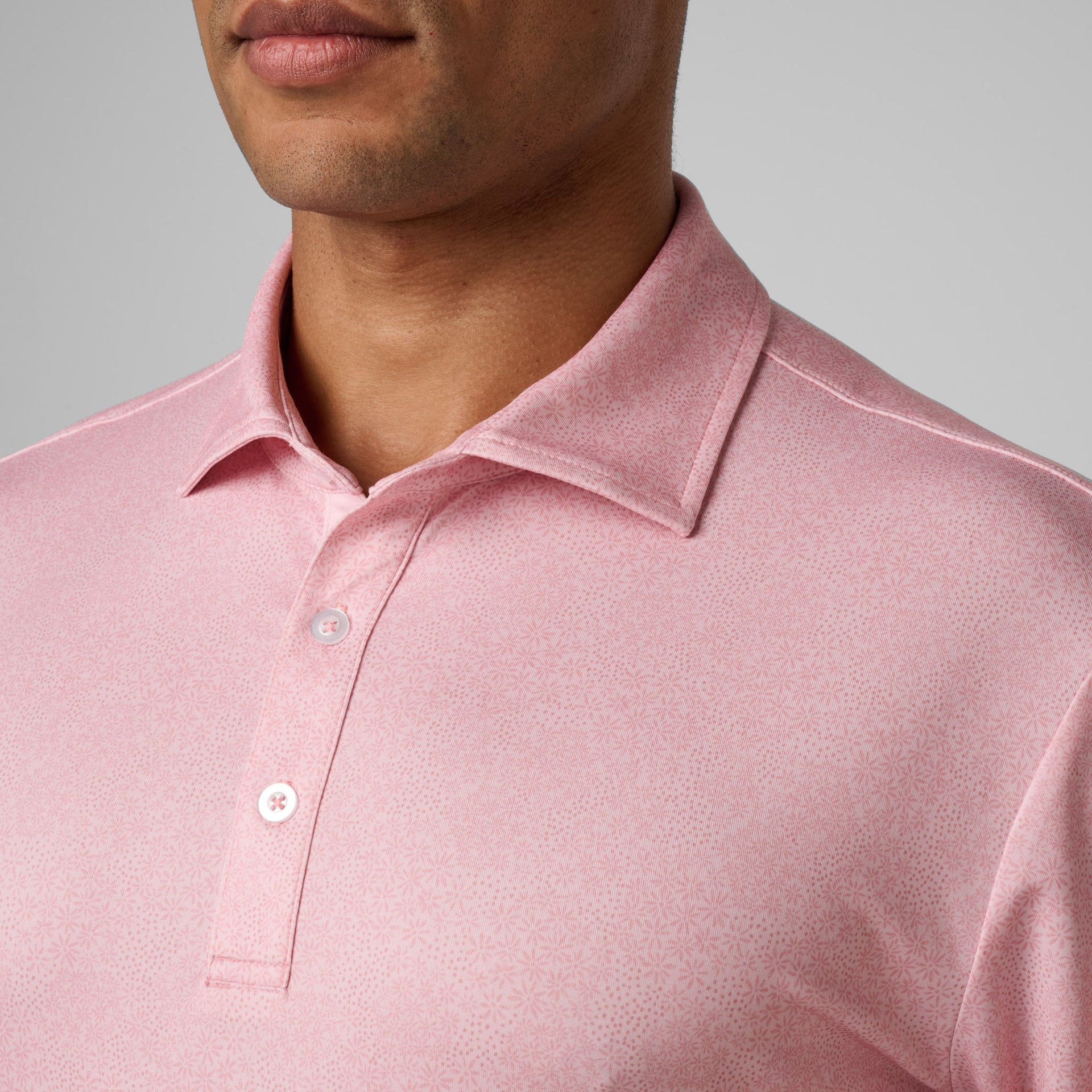 Man wearing a pink polo shirt with a subtle printed pattern and white buttons.