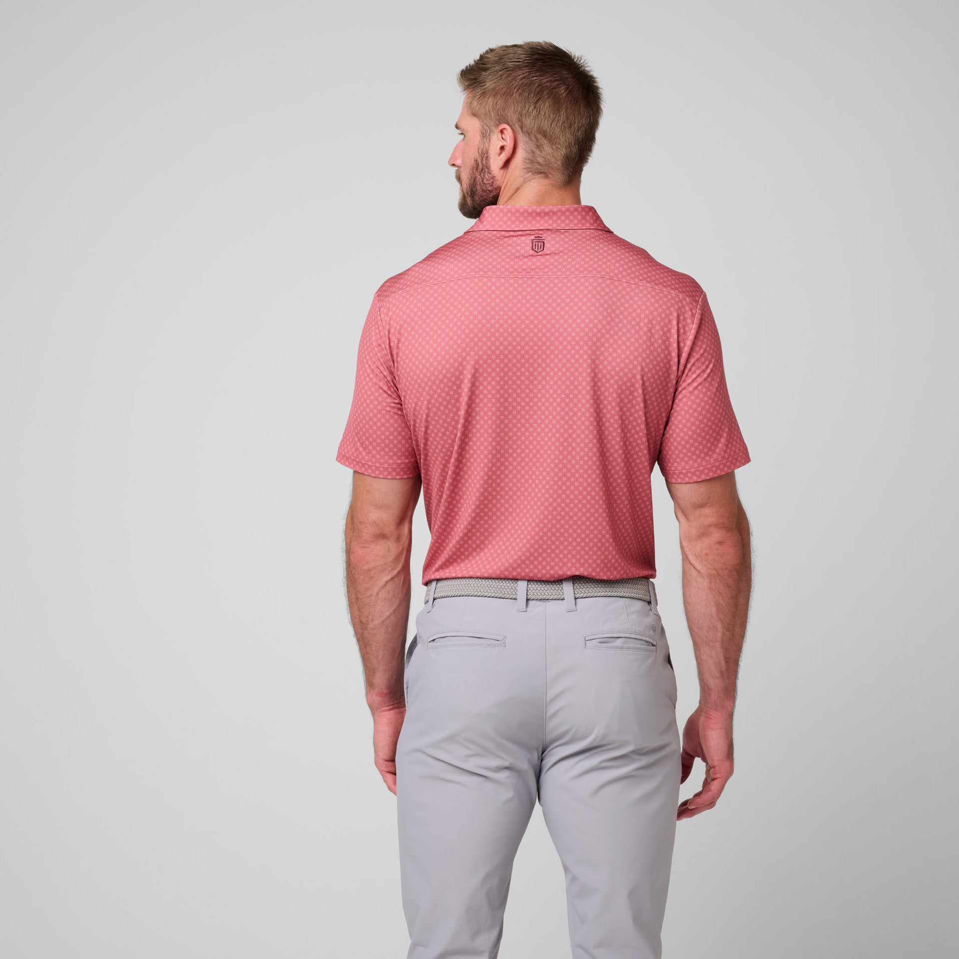 Man wearing pink printed polo shirt with small geometric pattern and gray pants, shown from back.