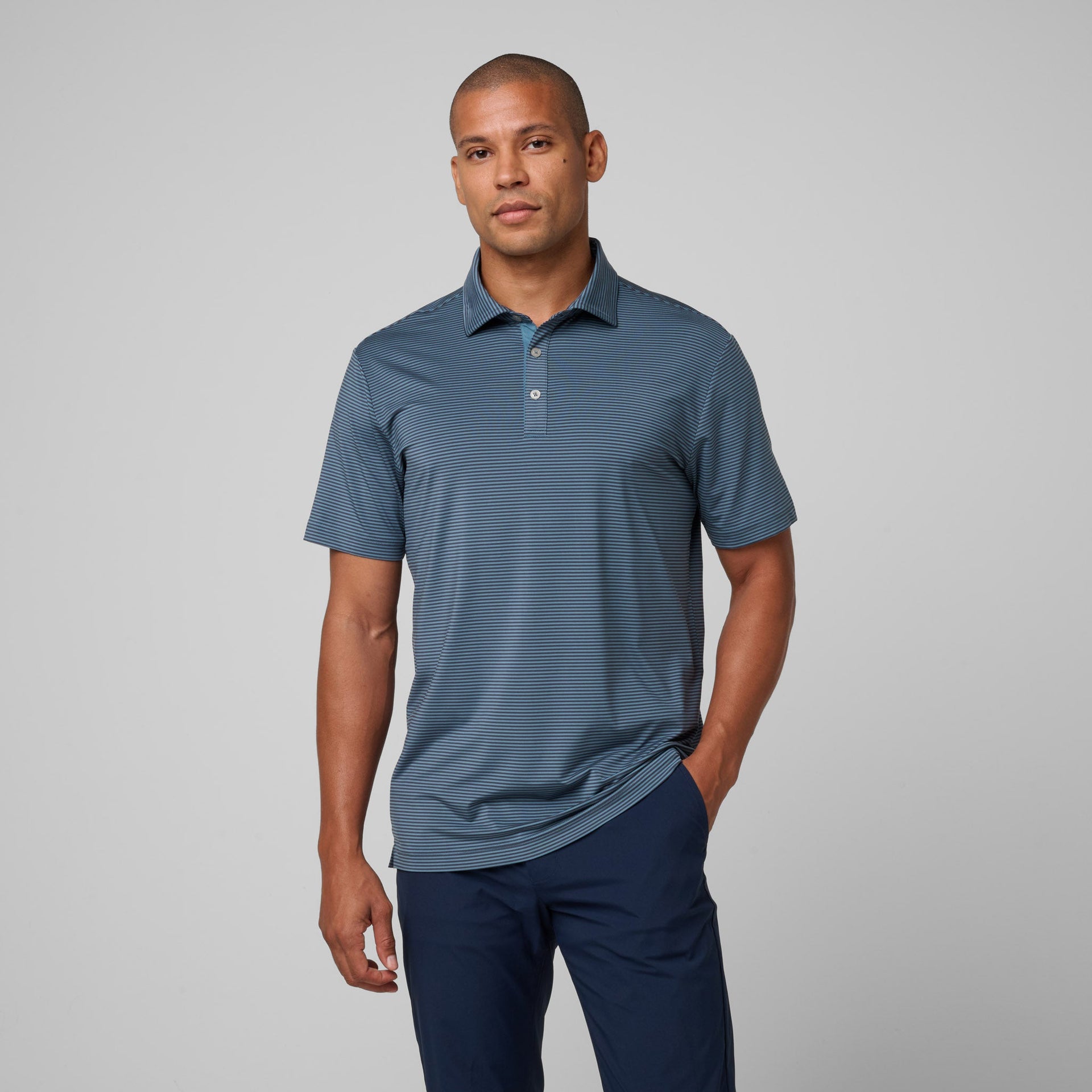 Man wearing blue striped polo shirt with collar and button placket paired with navy pants.