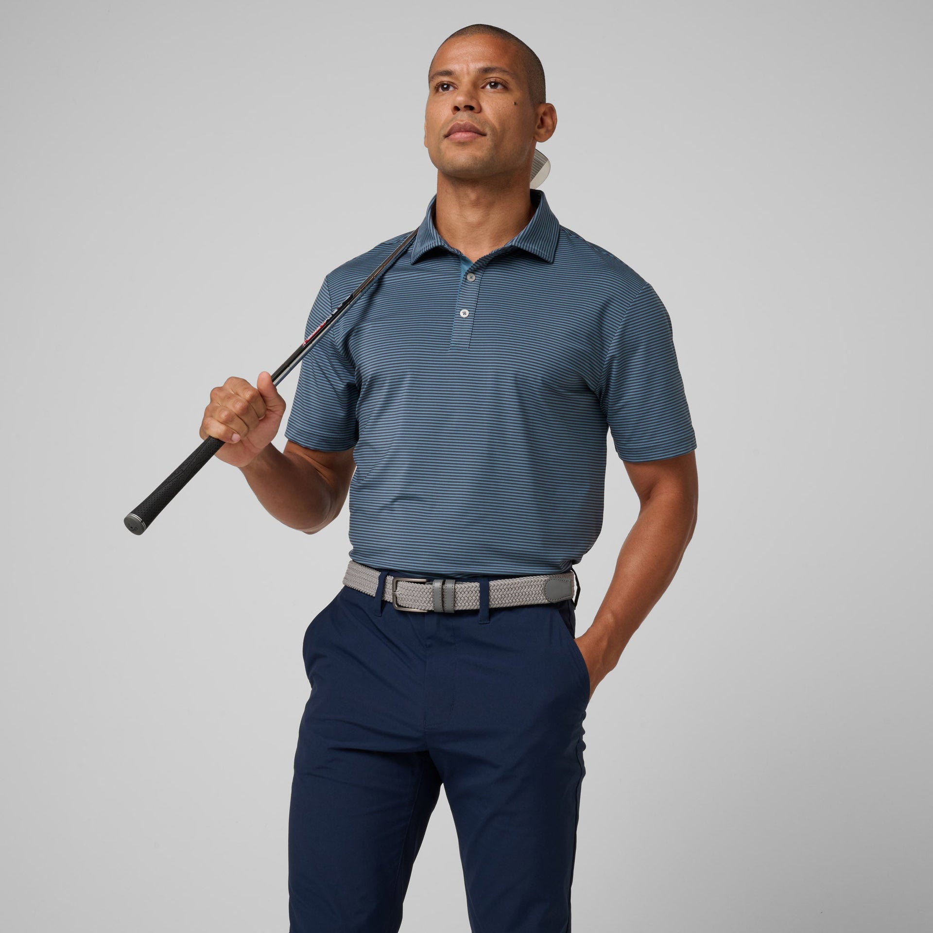 Man wearing blue striped short-sleeve polo shirt with white buttons and navy pants, holding a golf club.