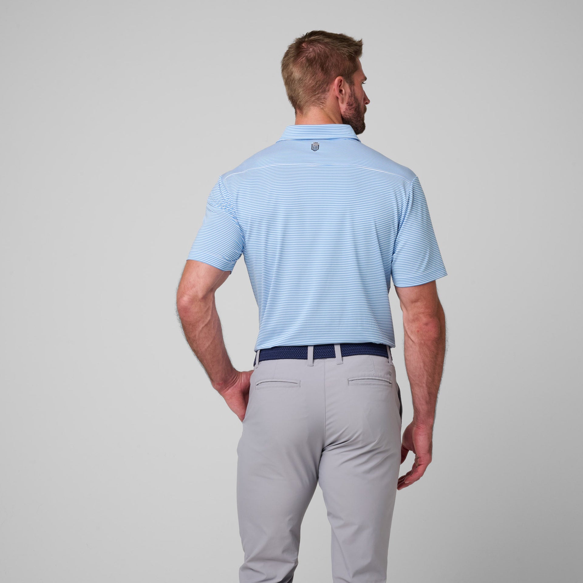 Light blue striped polo shirt with white horizontal lines, shown on male model with gray pants and navy belt.
