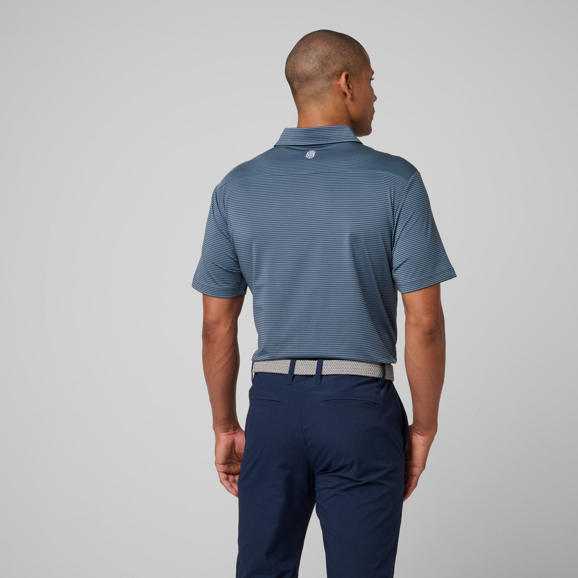 Man wearing blue striped polo shirt with collar and navy pants viewed from back.