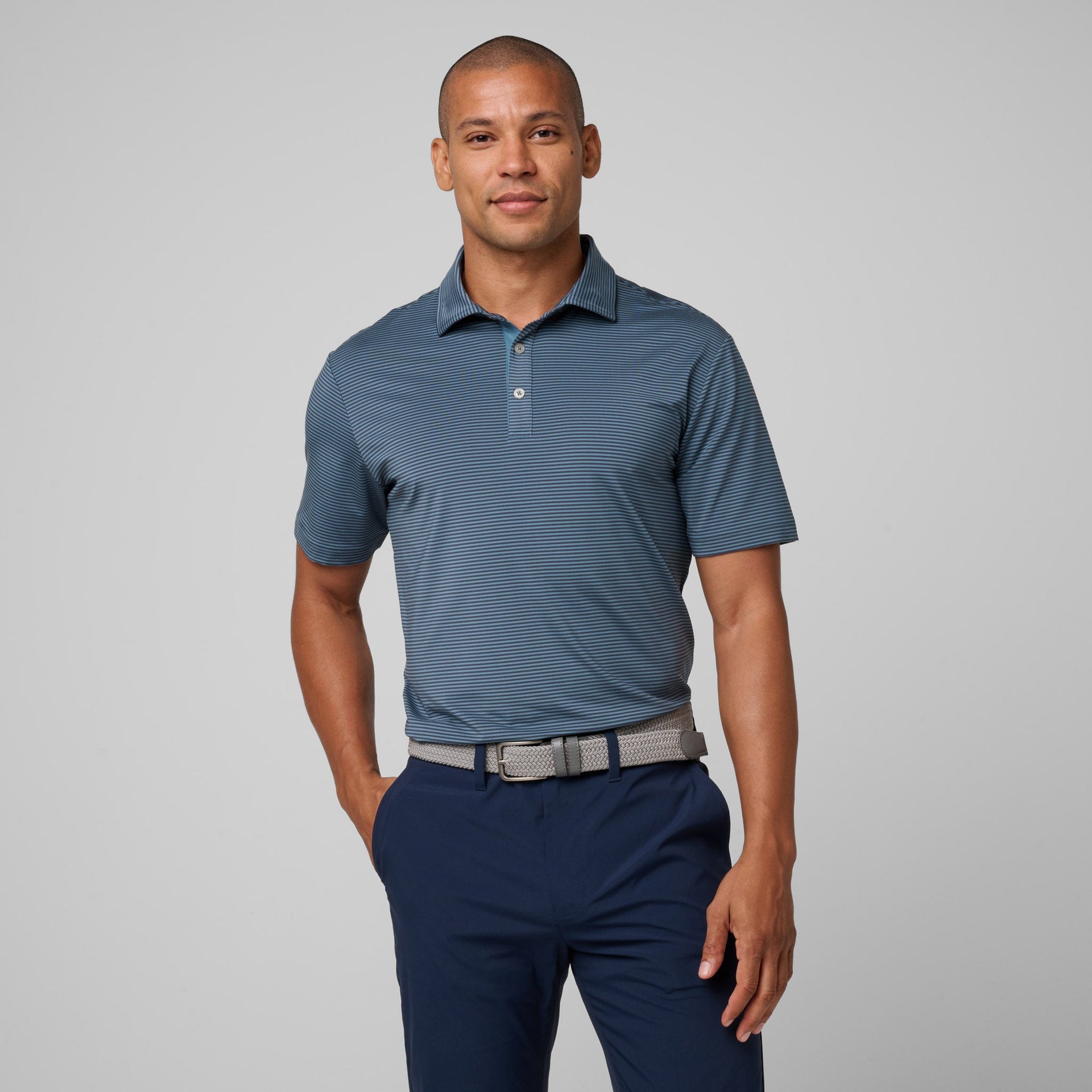 Man wearing blue striped polo shirt with collar and white buttons, paired with navy pants and gray belt.