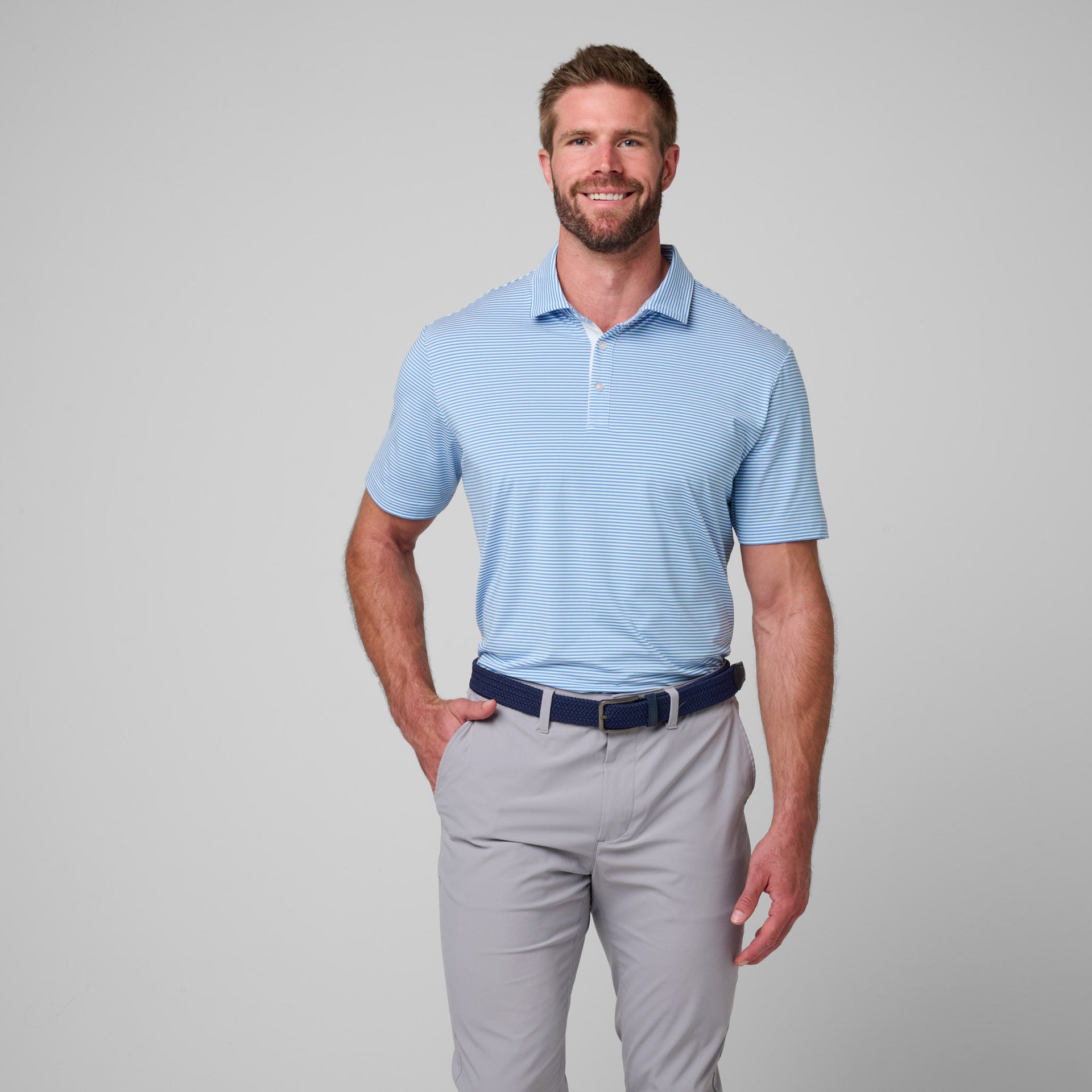 Man wearing light blue striped polo shirt with white pinstripes and gray pants with navy belt.