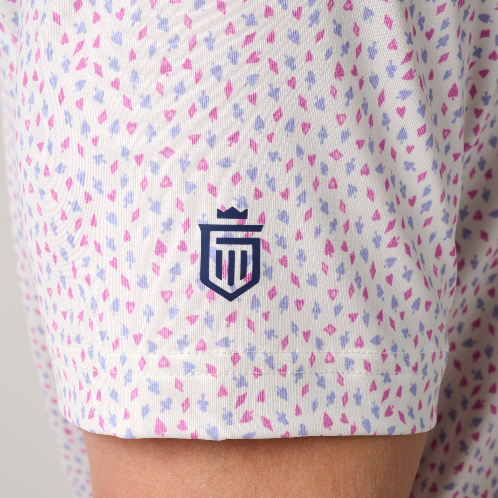 White polo shirt with allover pink and purple geometric pattern and navy embroidered crest logo.