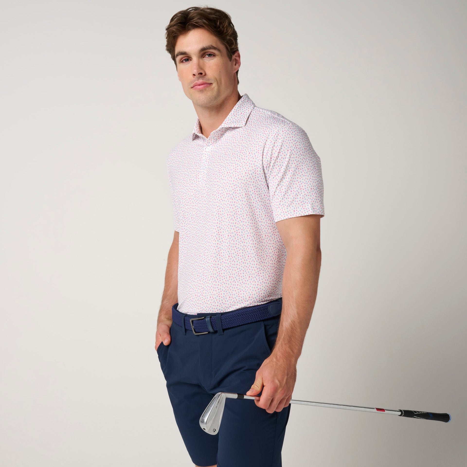 Man wearing light pink polo with small geometric pattern and navy shorts with belt.