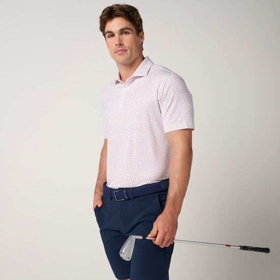 Man wearing light pink polo with small geometric pattern and navy shorts with belt.