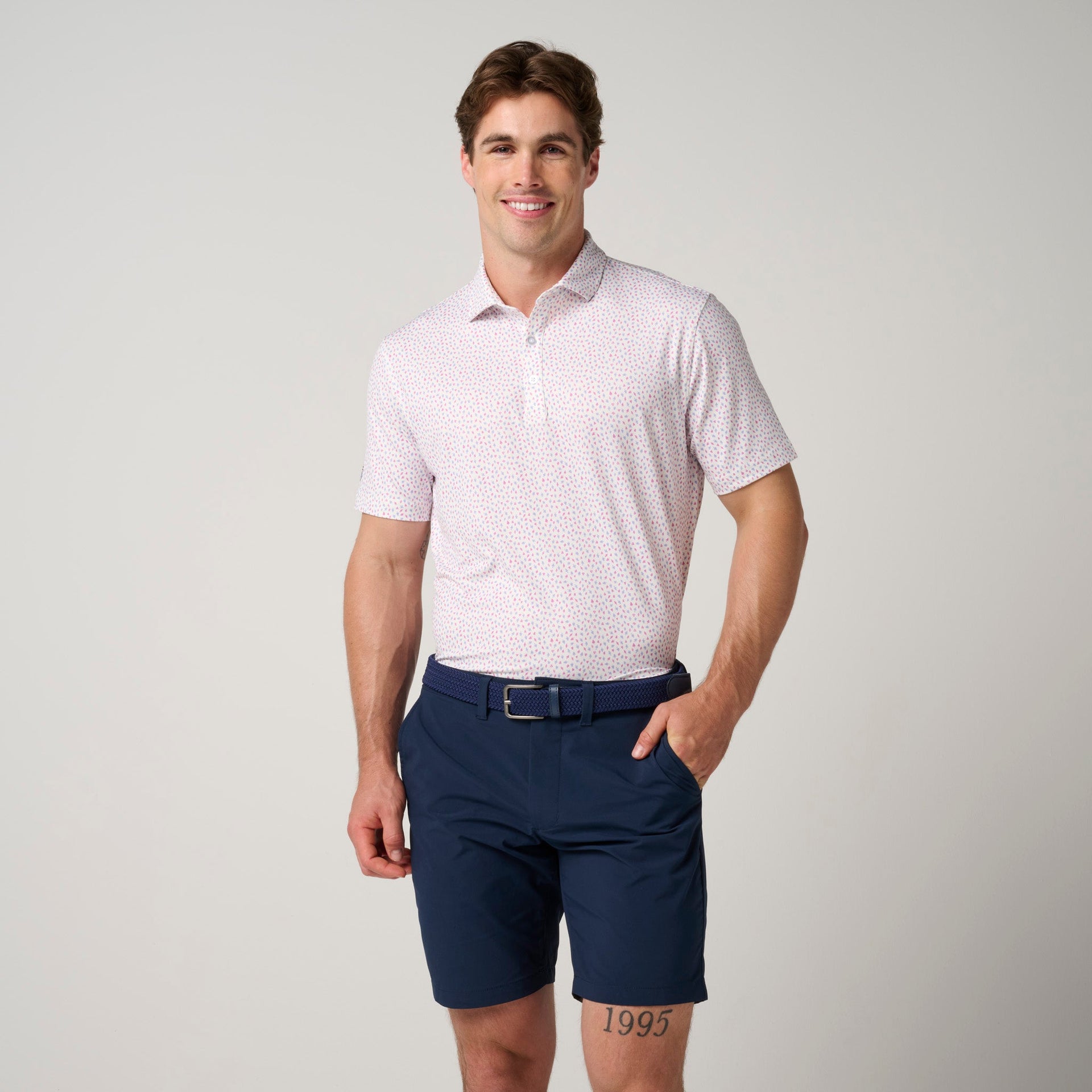 Man wearing light pink patterned short-sleeve polo shirt with navy shorts and belt.