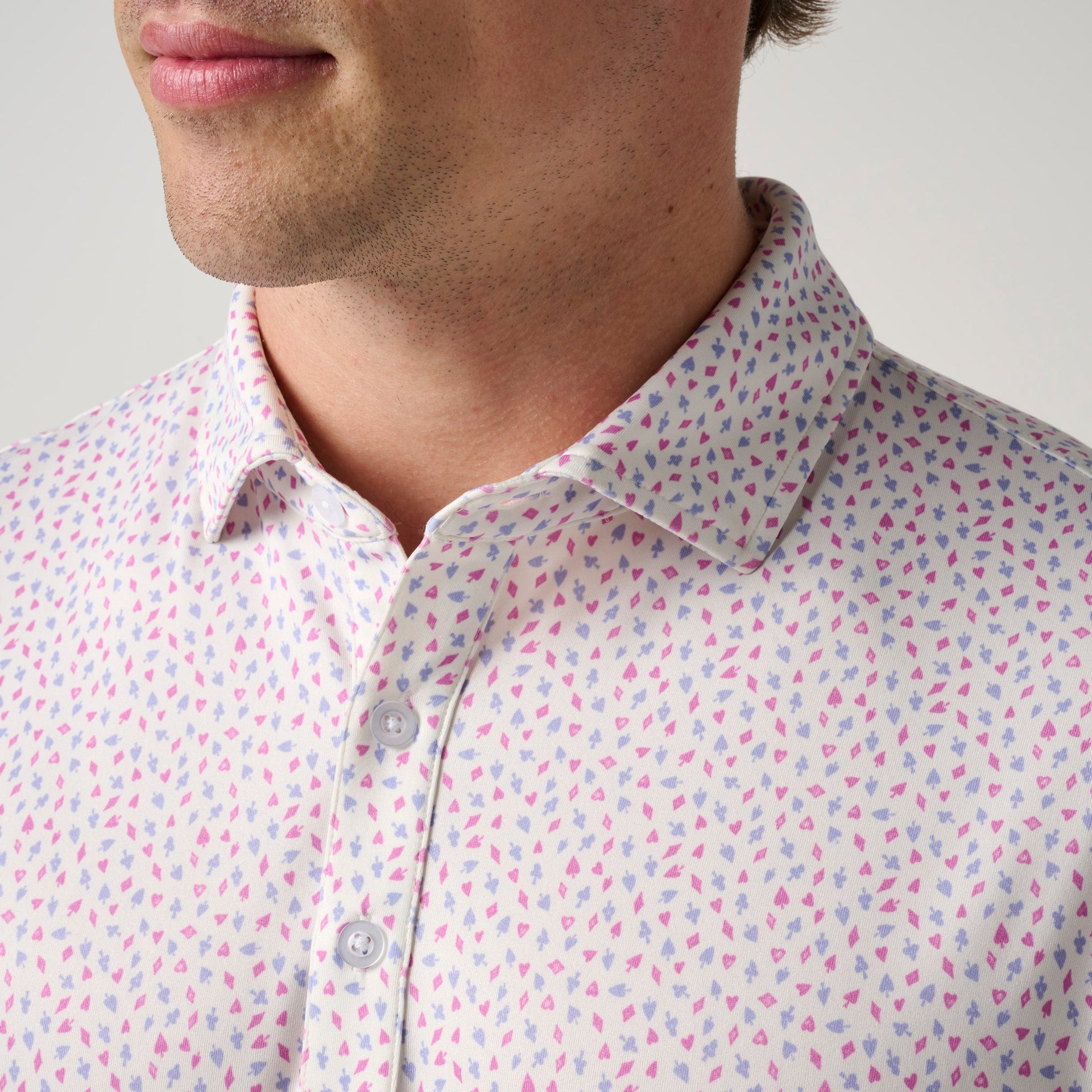 Man wearing white polo shirt with pink and purple scattered heart pattern and button front closure.