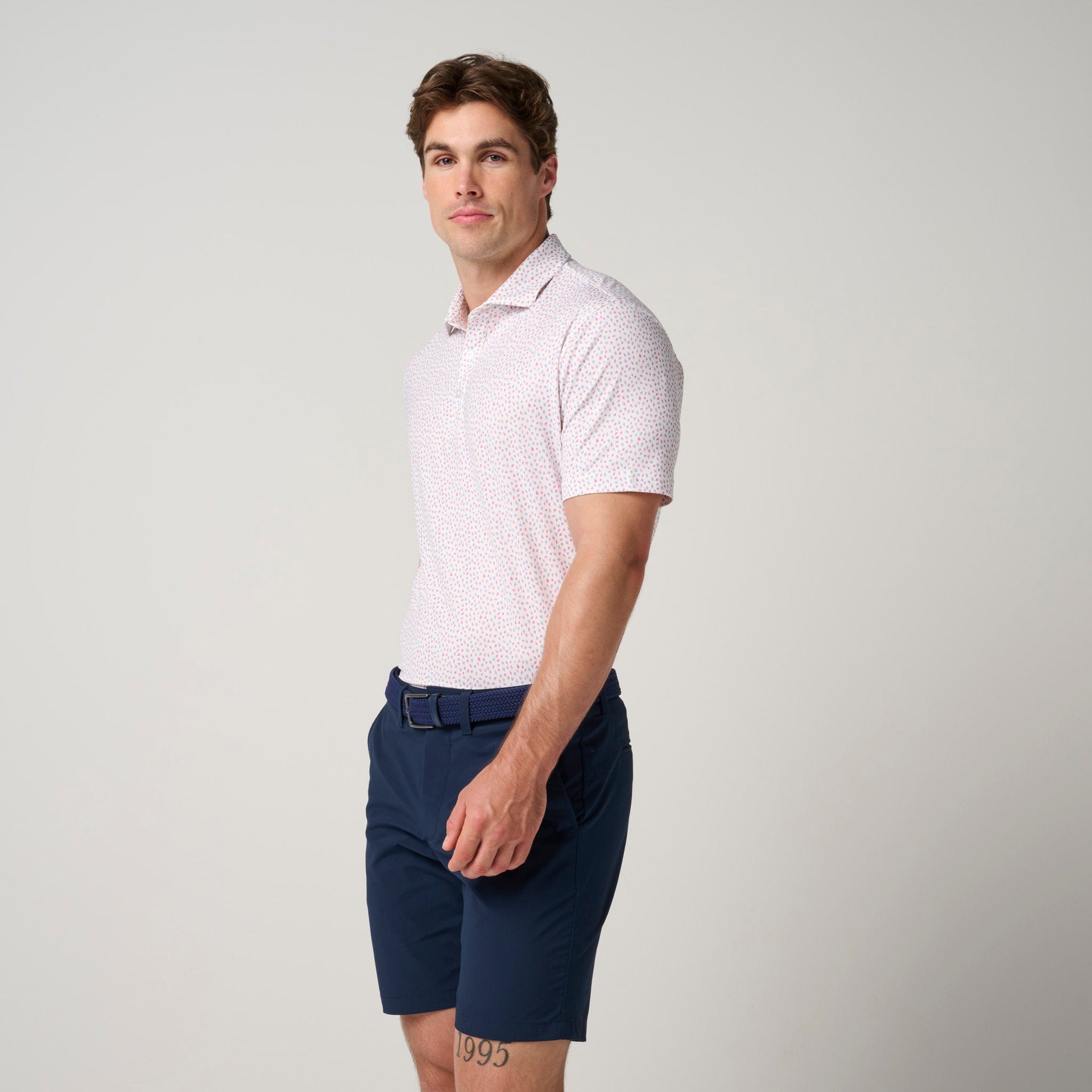 Man wearing light pink polo shirt with small pattern and navy shorts with belt.