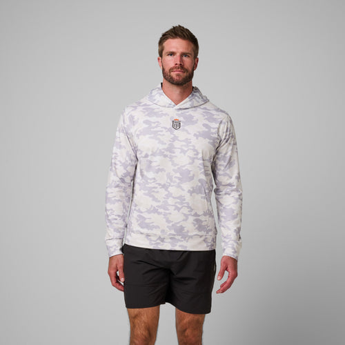 Man wearing light gray and white camouflage hoodie with small chest logo and black shorts.
