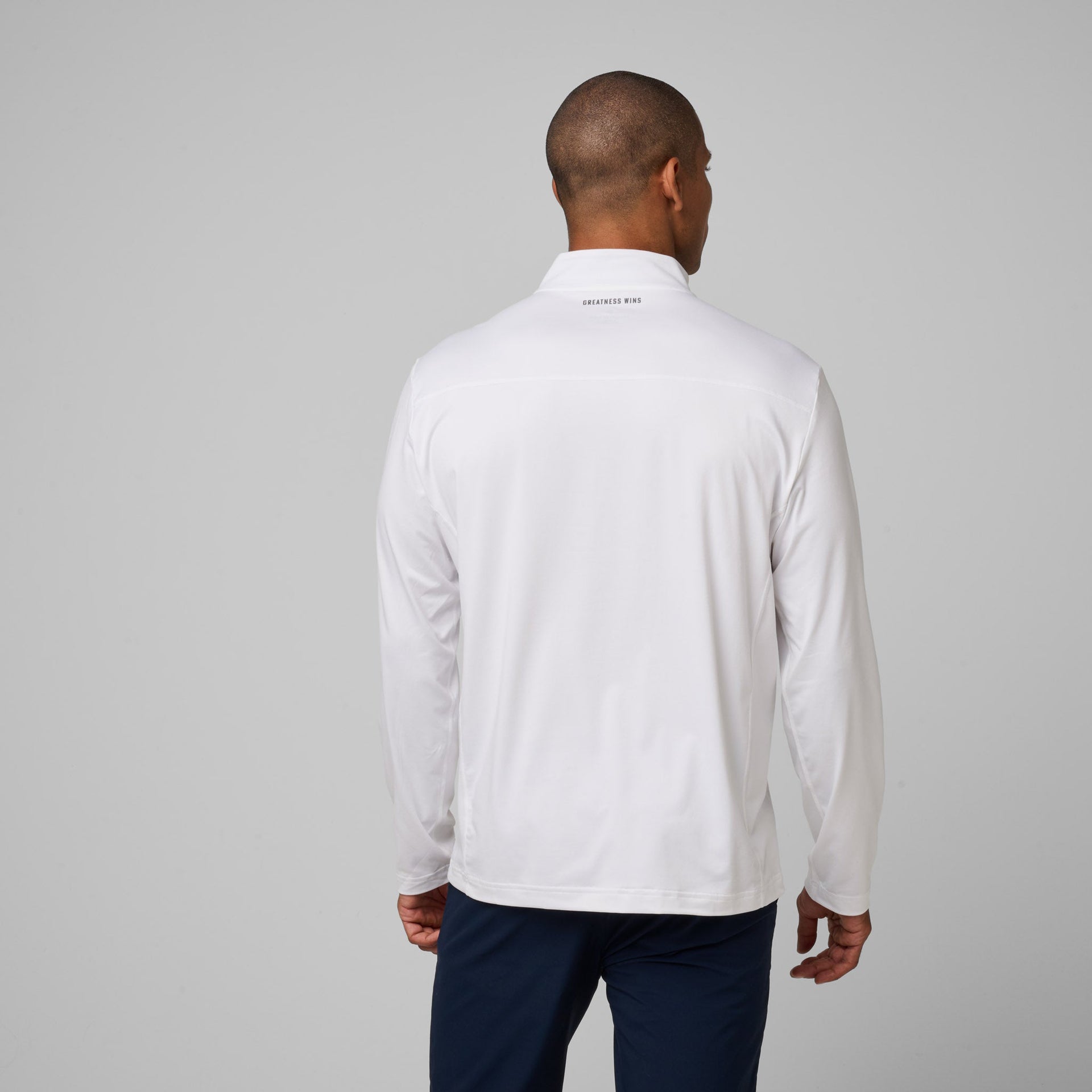 Man wearing white quarter zip pullover with navy pants, shown from back view.