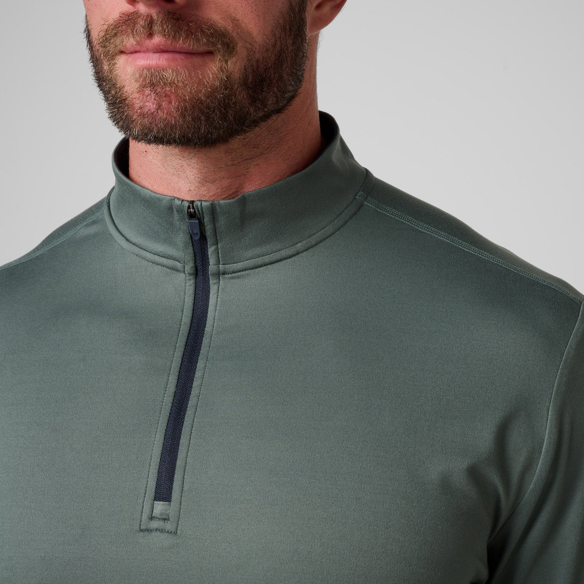 Sage green quarter-zip pullover with dark navy contrast zip detail on chest.