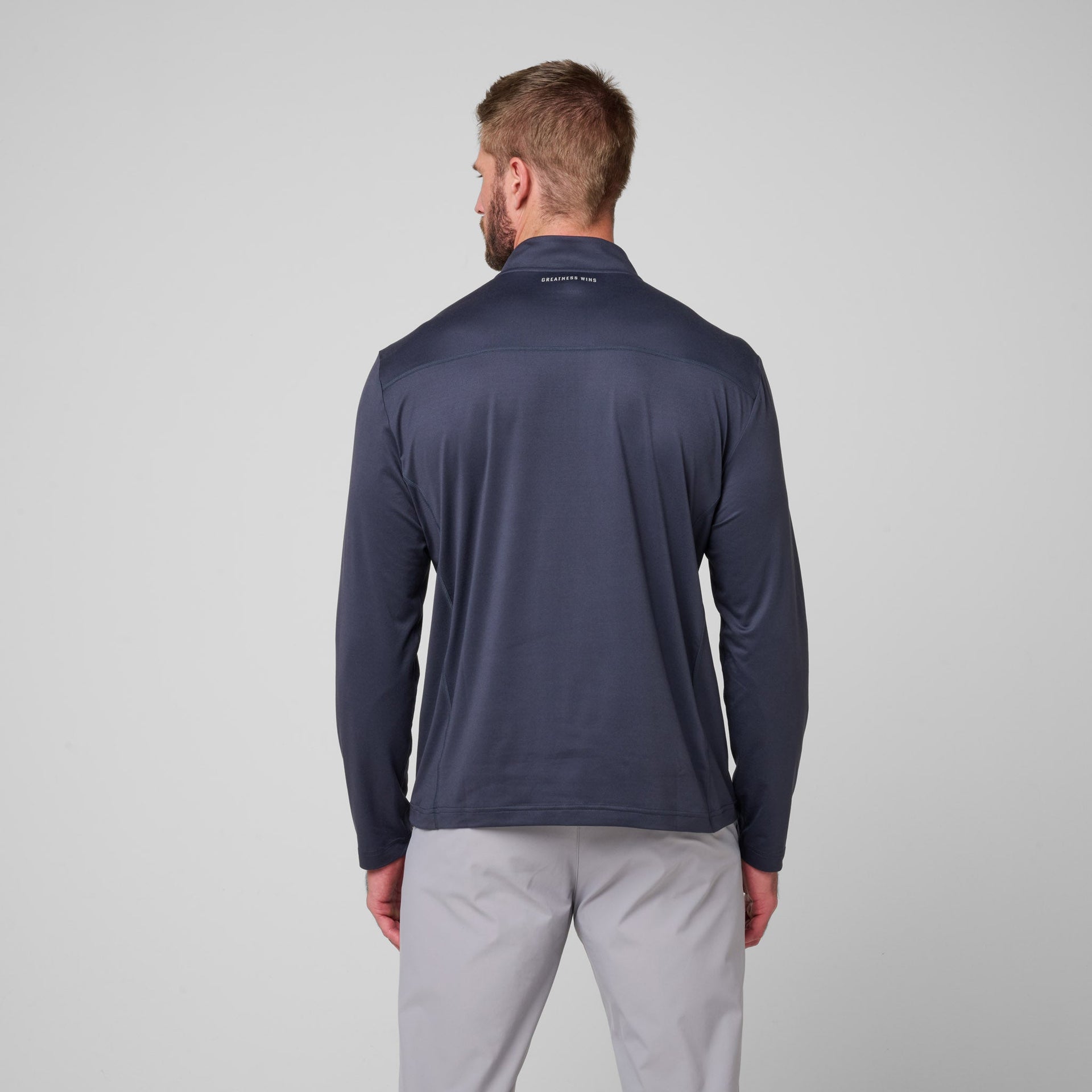 Man wearing navy quarter-zip pullover with long sleeves and light gray pants, shown from behind.