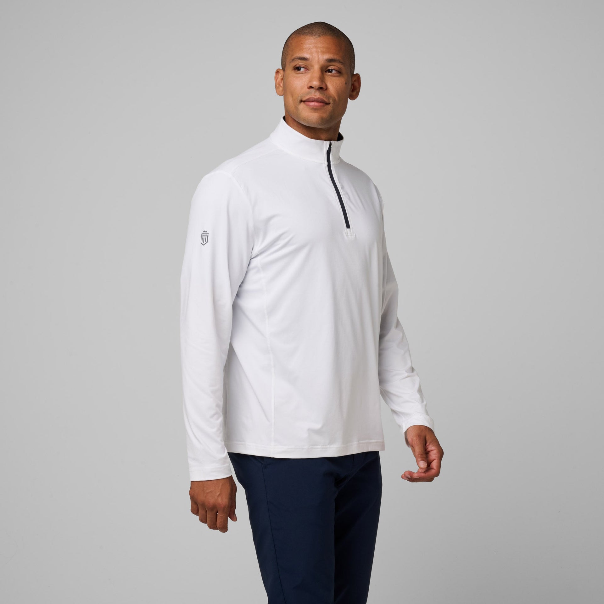 Man wearing white long-sleeve quarter-zip pullover with navy trim and small chest logo, paired with dark navy pants.