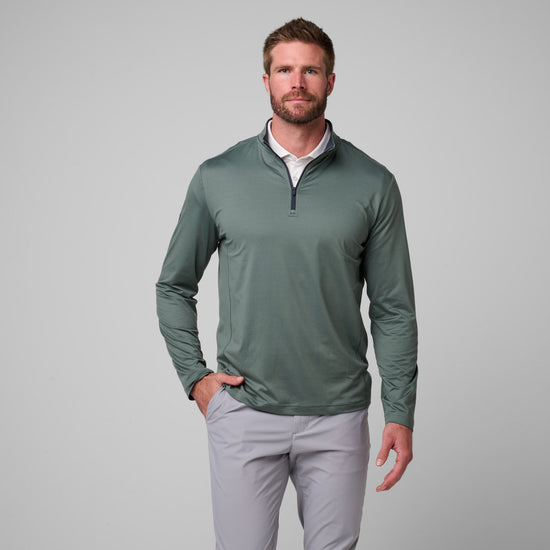 Sage green quarter zip pullover with dark trim worn with light gray pants.