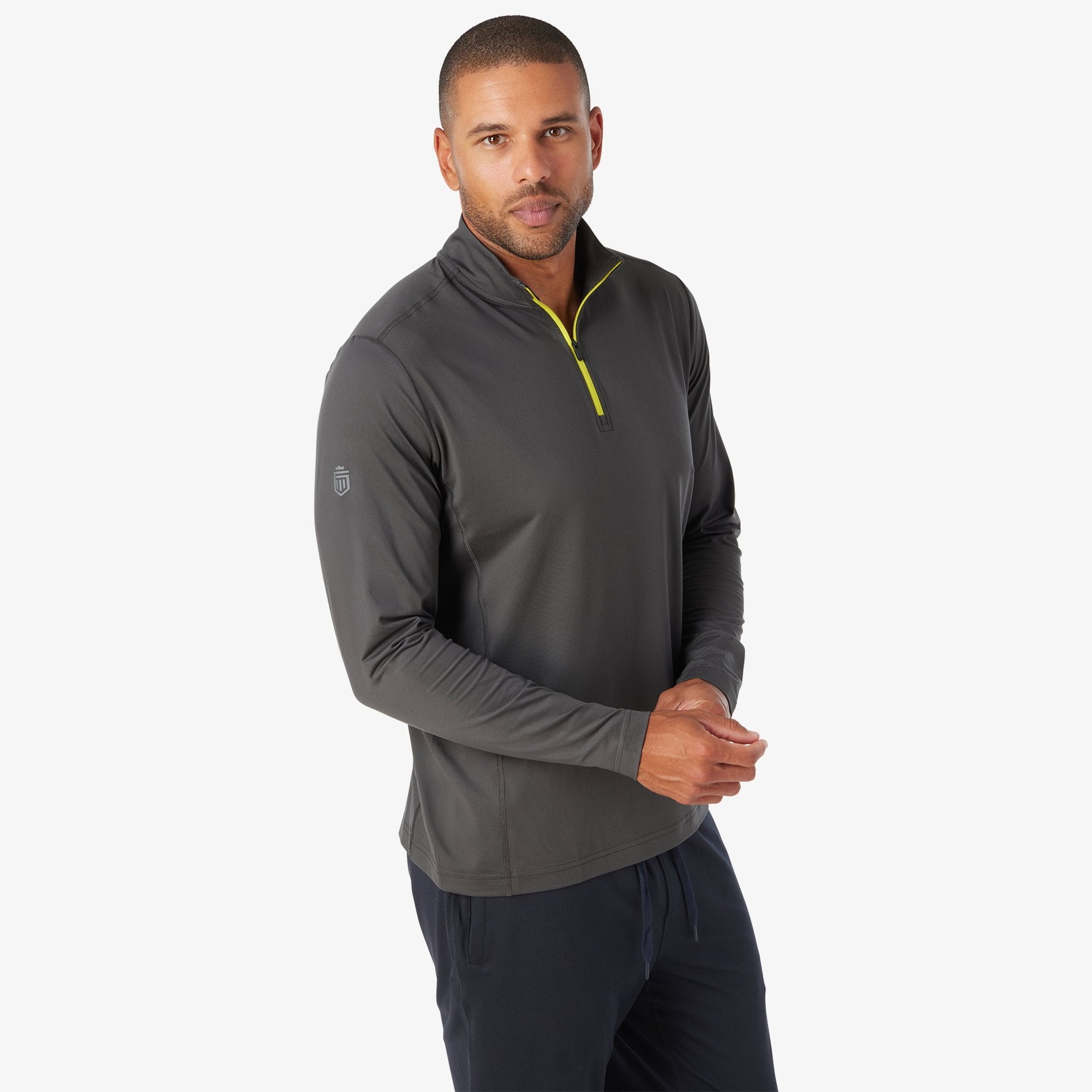 Man wearing charcoal quarter zip pullover with yellow trim and small chest logo, paired with dark pants.