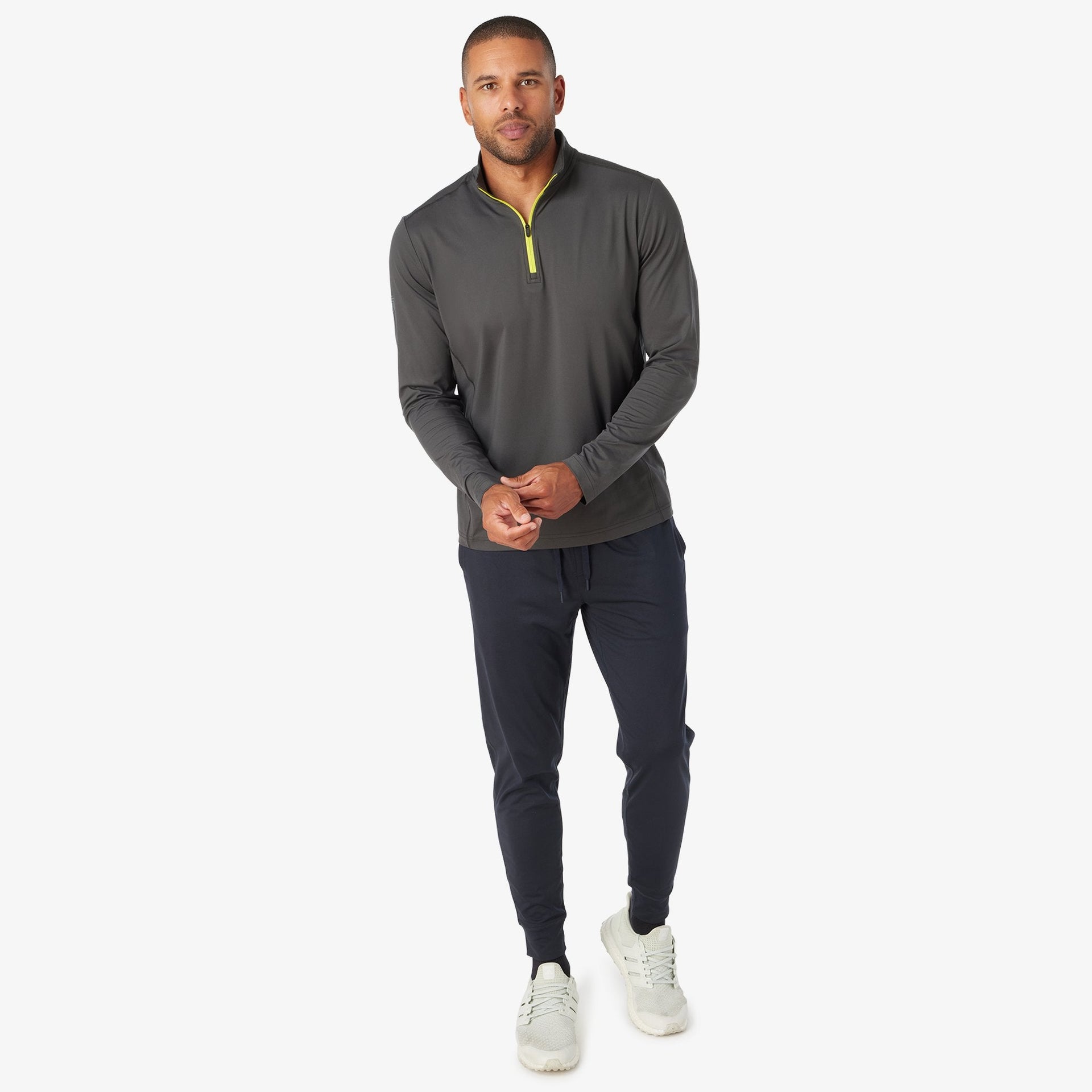 Man wearing charcoal quarter zip pullover with yellow zipper and dark navy joggers.