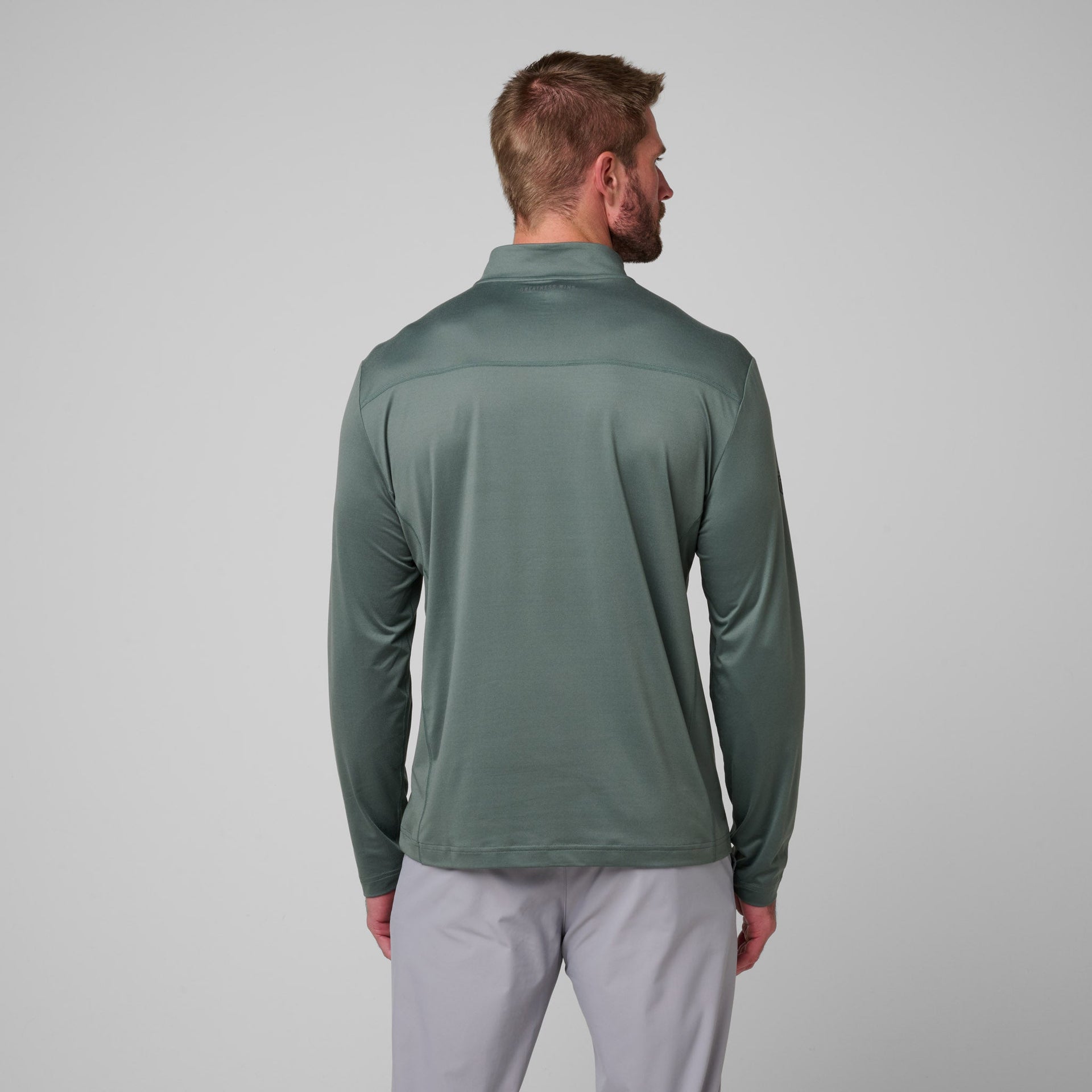 Man wearing sage green quarter-zip pullover with long sleeves and light gray pants, shown from back view.