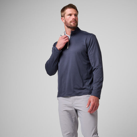 Man wearing navy quarter-zip pullover with light gray pants against neutral background.