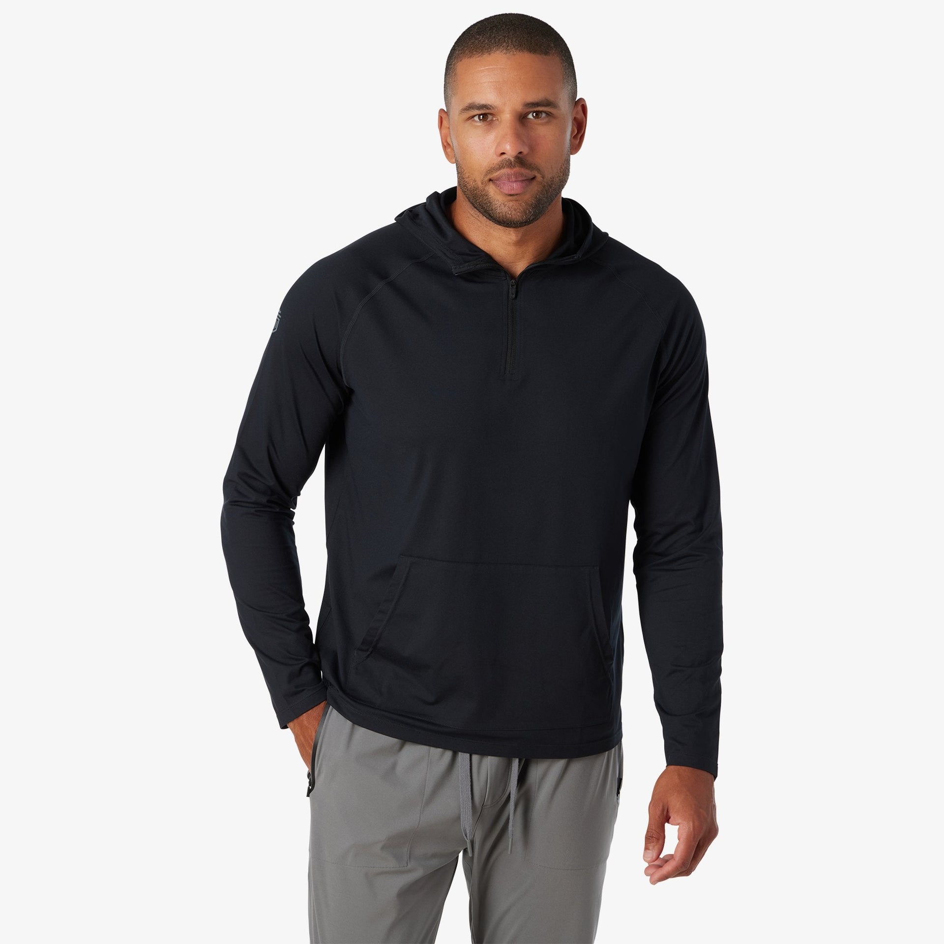 Man wearing black quarter-zip hooded sweatshirt with long sleeves and gray pants.