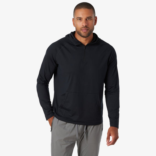 Man wearing black quarter-zip hooded sweatshirt with long sleeves and gray pants.