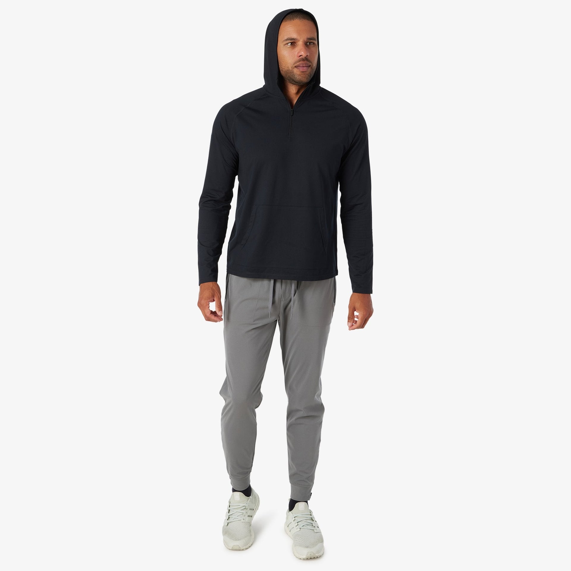 Black quarter zip hoodie with long sleeves worn with gray joggers and light sneakers.