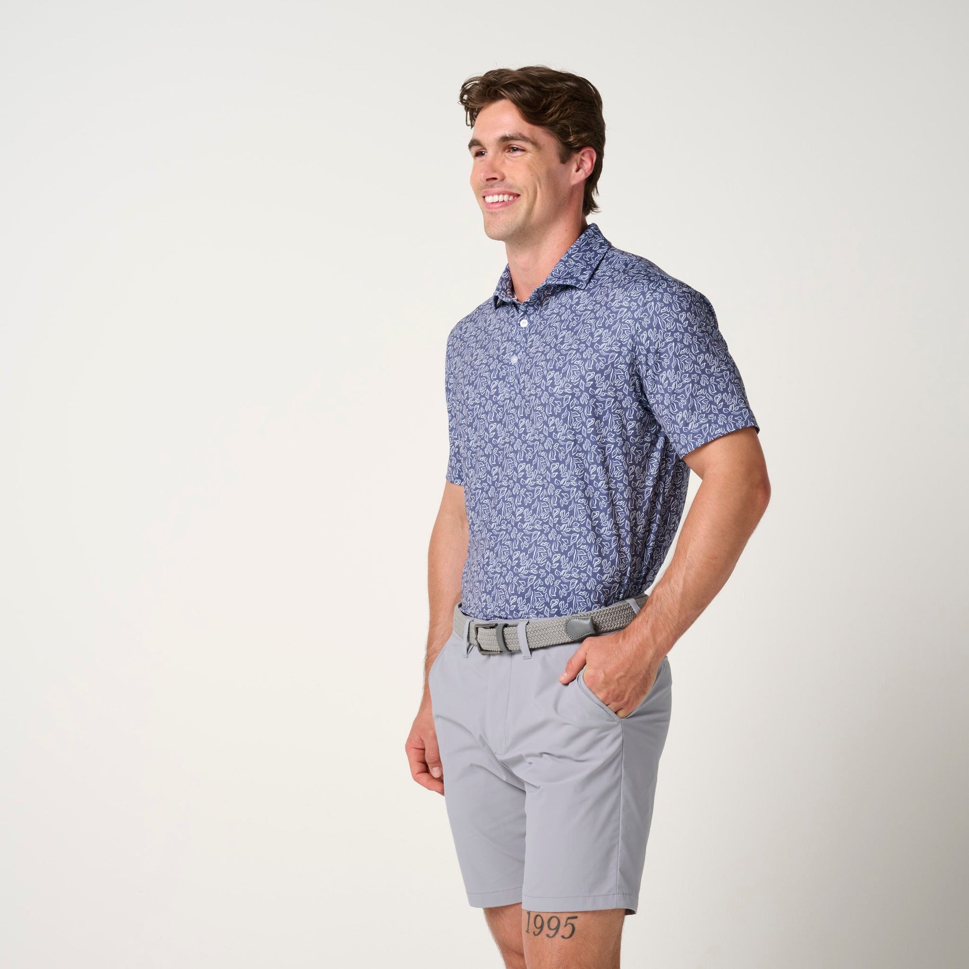 Man wearing blue floral polo shirt with short sleeves and gray shorts with tan belt.