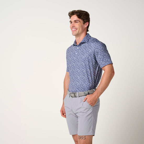 Man wearing blue floral polo shirt with short sleeves and gray shorts with tan belt.